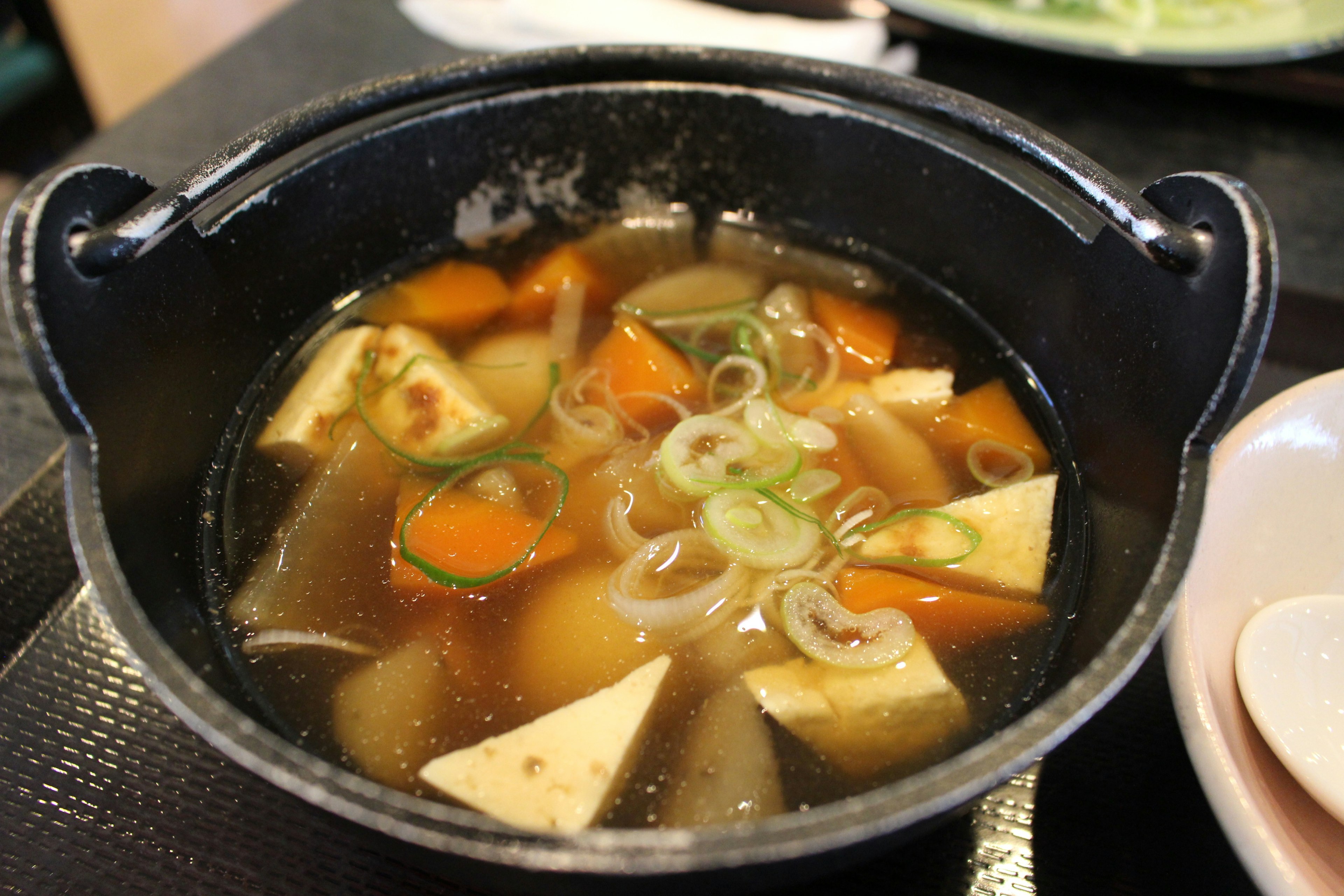 A hearty soup in a black pot featuring tofu and various vegetables