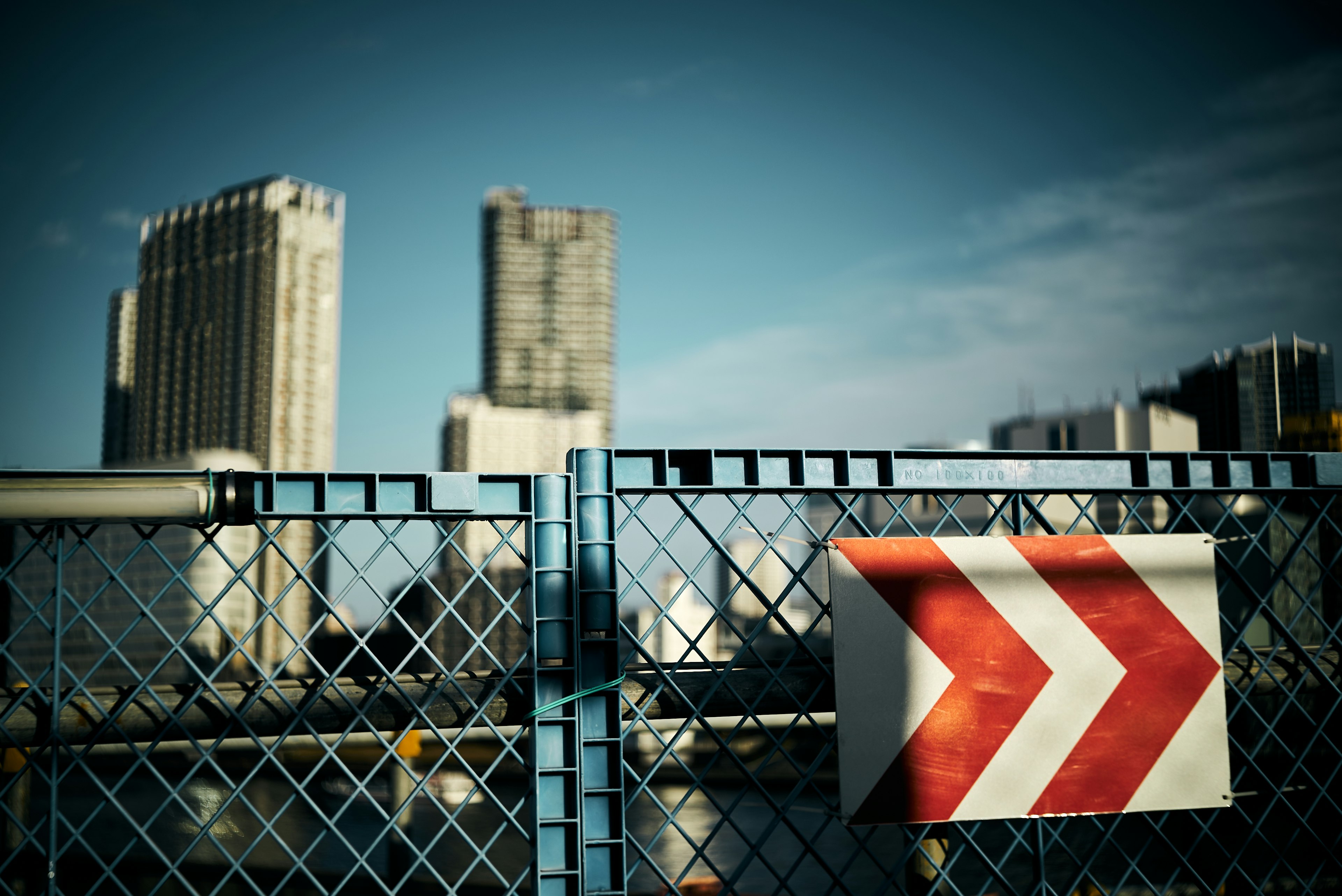 A fence with red arrow signs against a city skyline under a blue sky