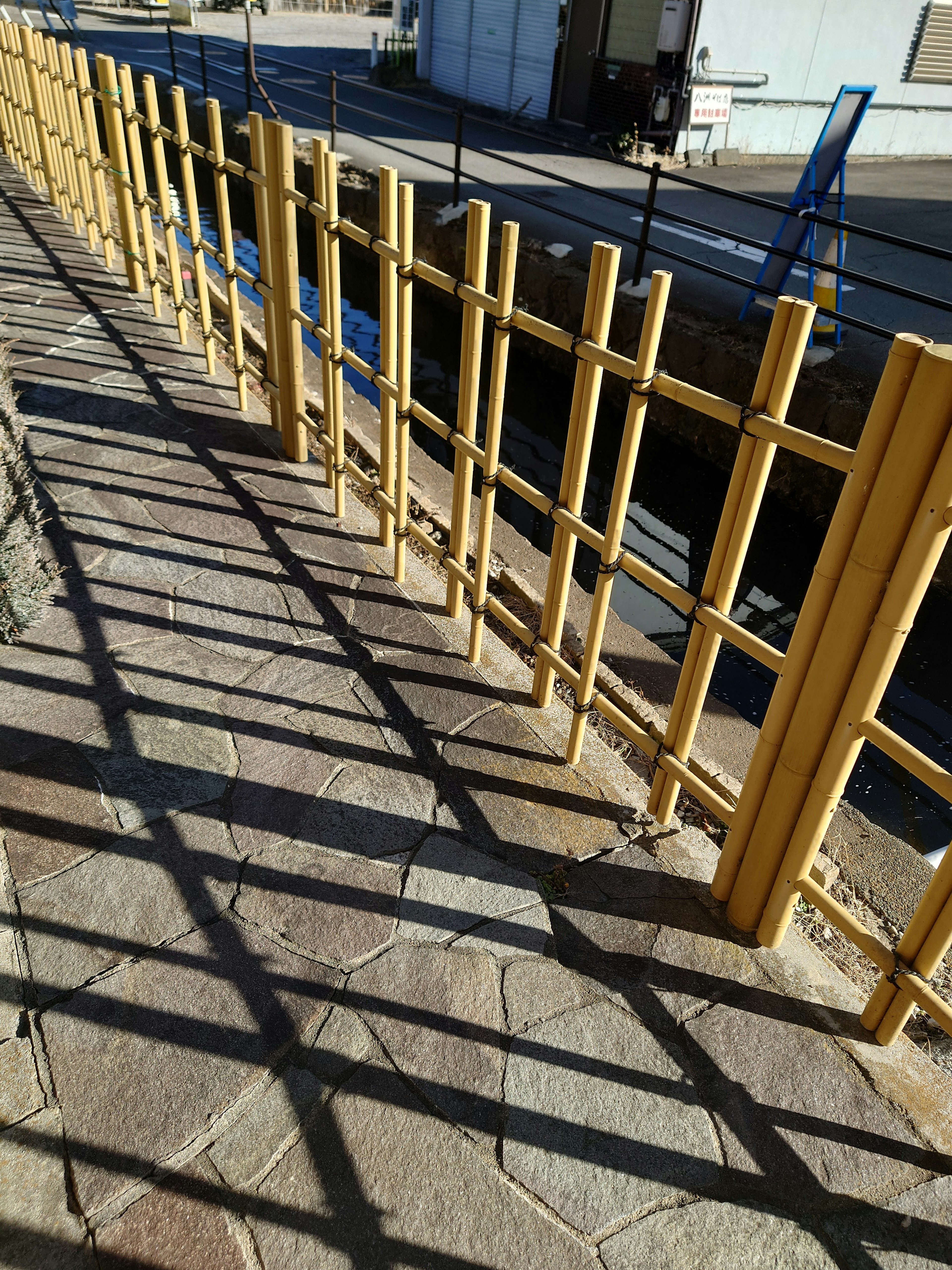 Photo d'un chemin pavé avec une clôture jaune et des ombres distinctes