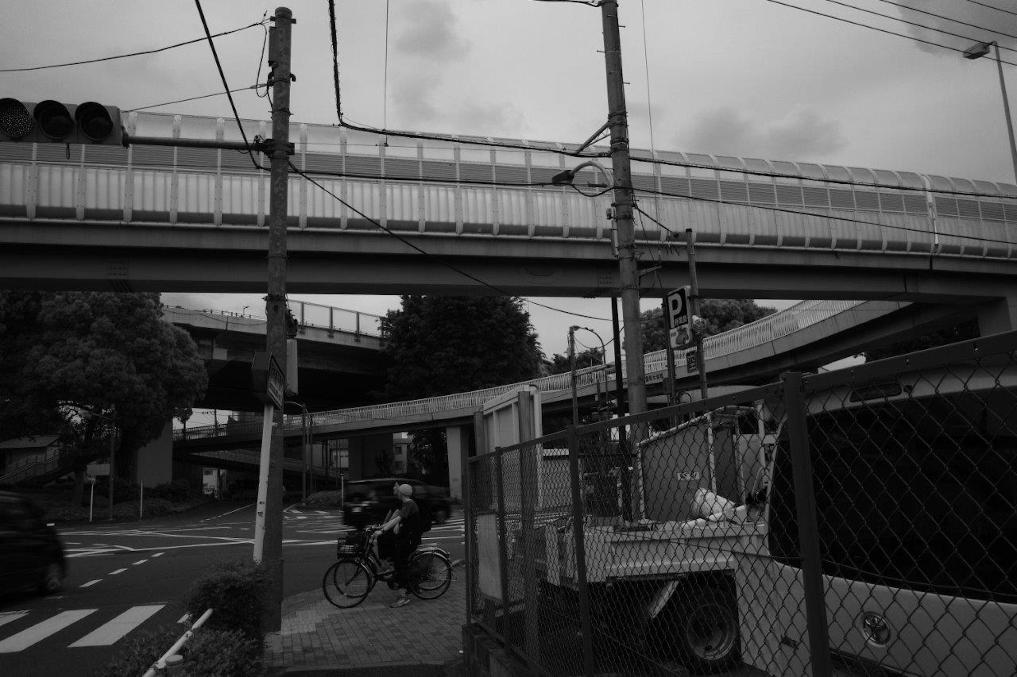 Black and white urban scene featuring an elevated bridge and a cyclist