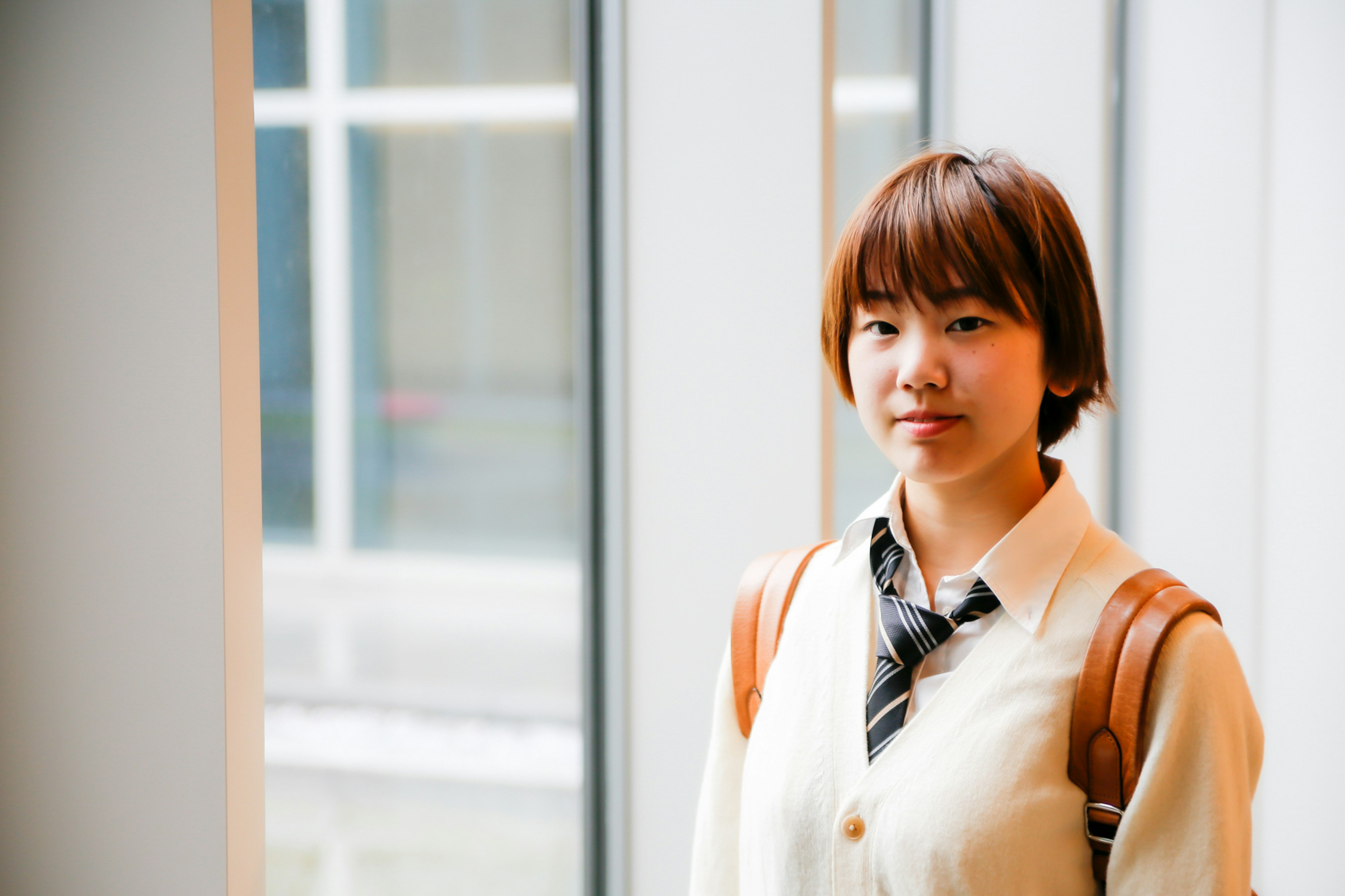 A young woman with brown hair standing near a window wearing casual attire