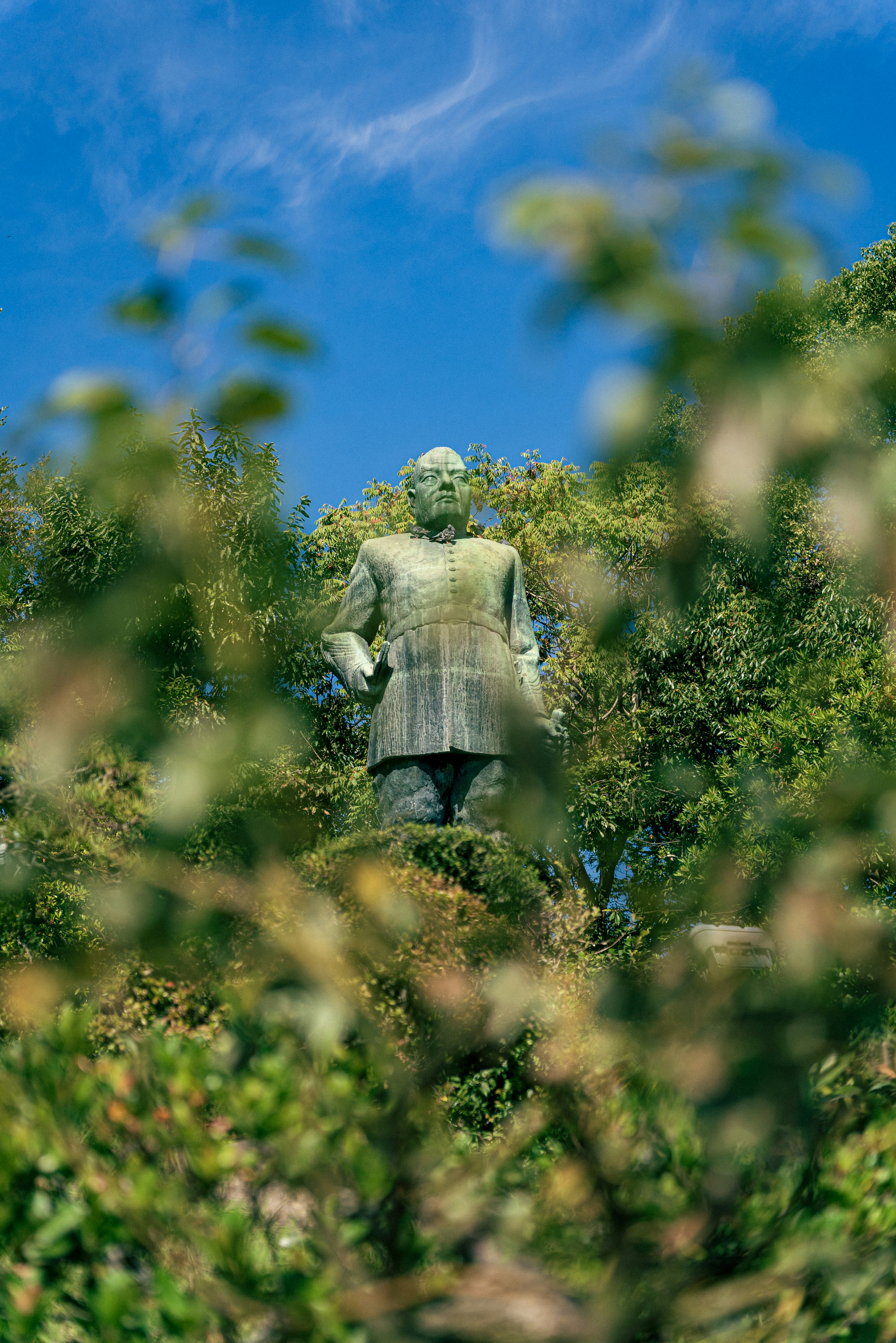 Large statue visible through green foliage under a blue sky