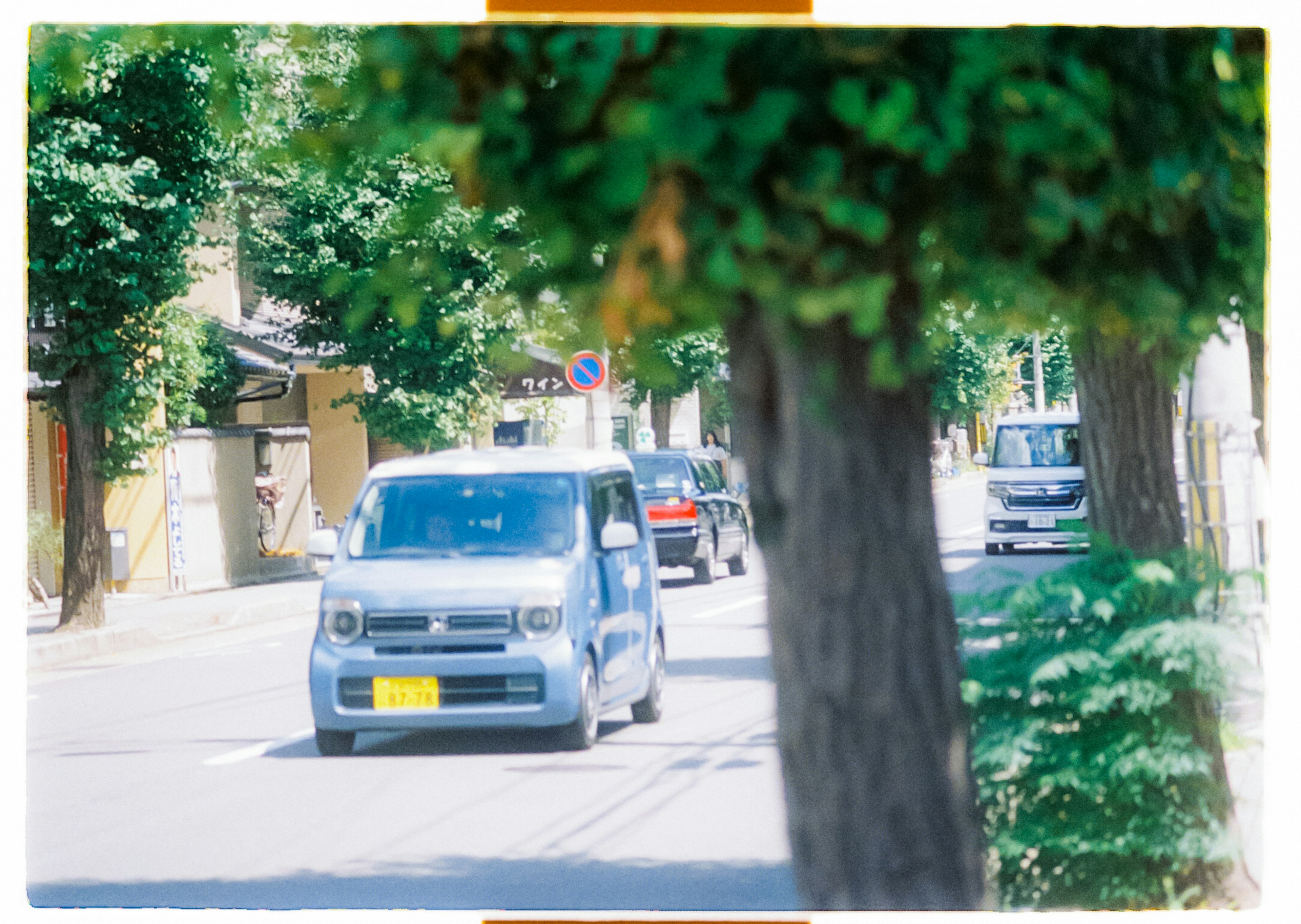 A blue car driving down a quiet street lined with green trees