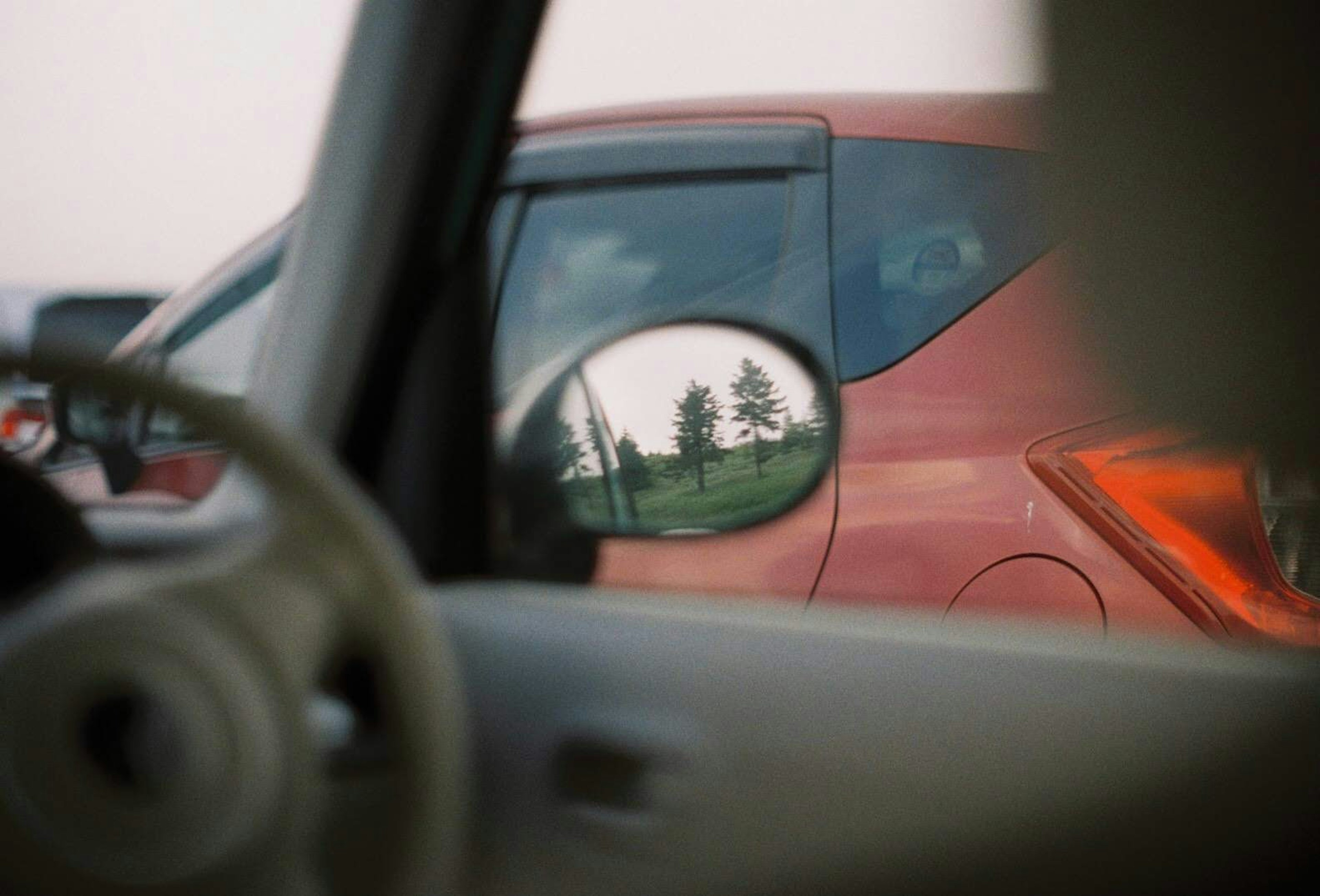 Reflejo de un coche rojo en el espejo lateral con un volante a la vista