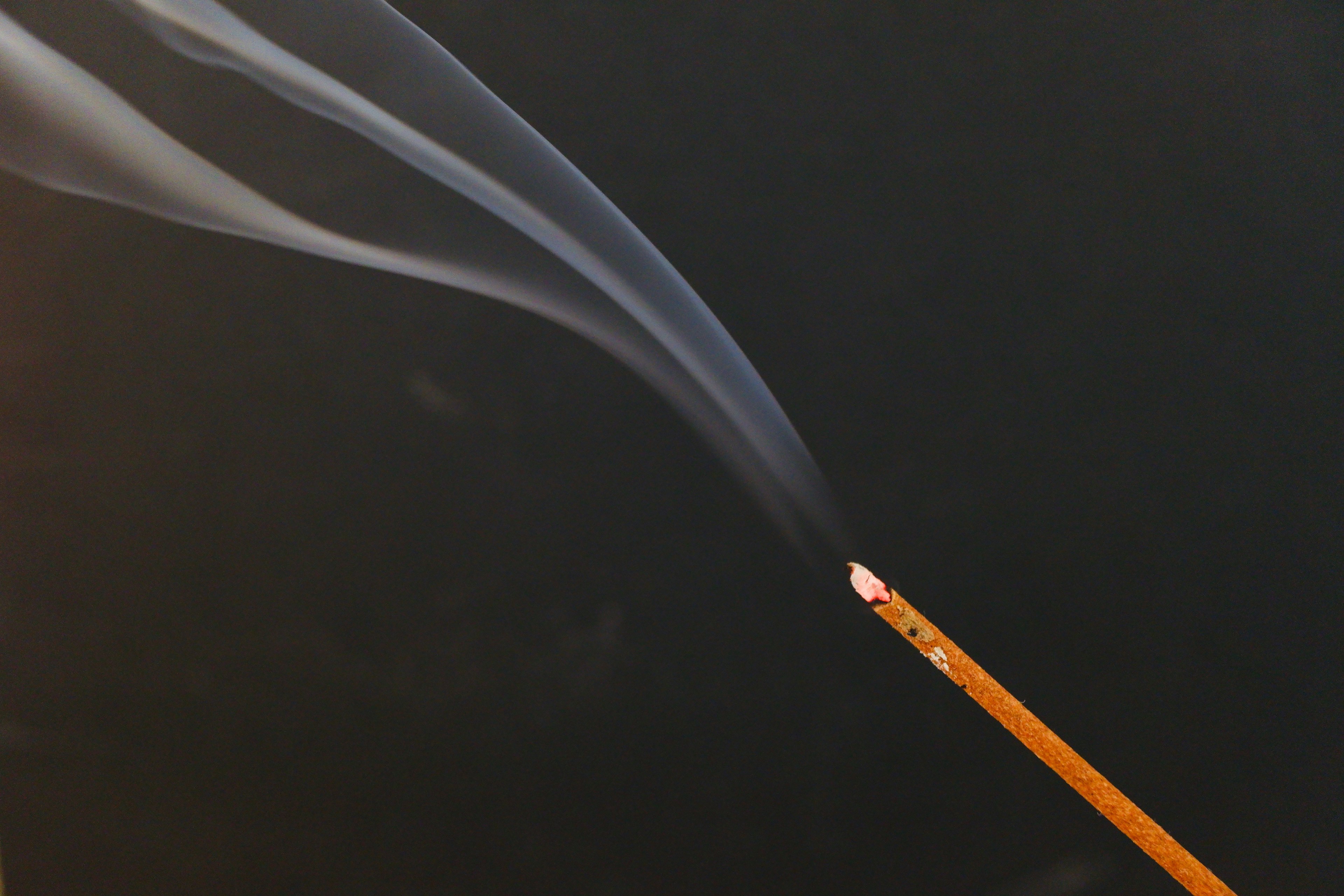 Incense stick emitting smoke against a black background