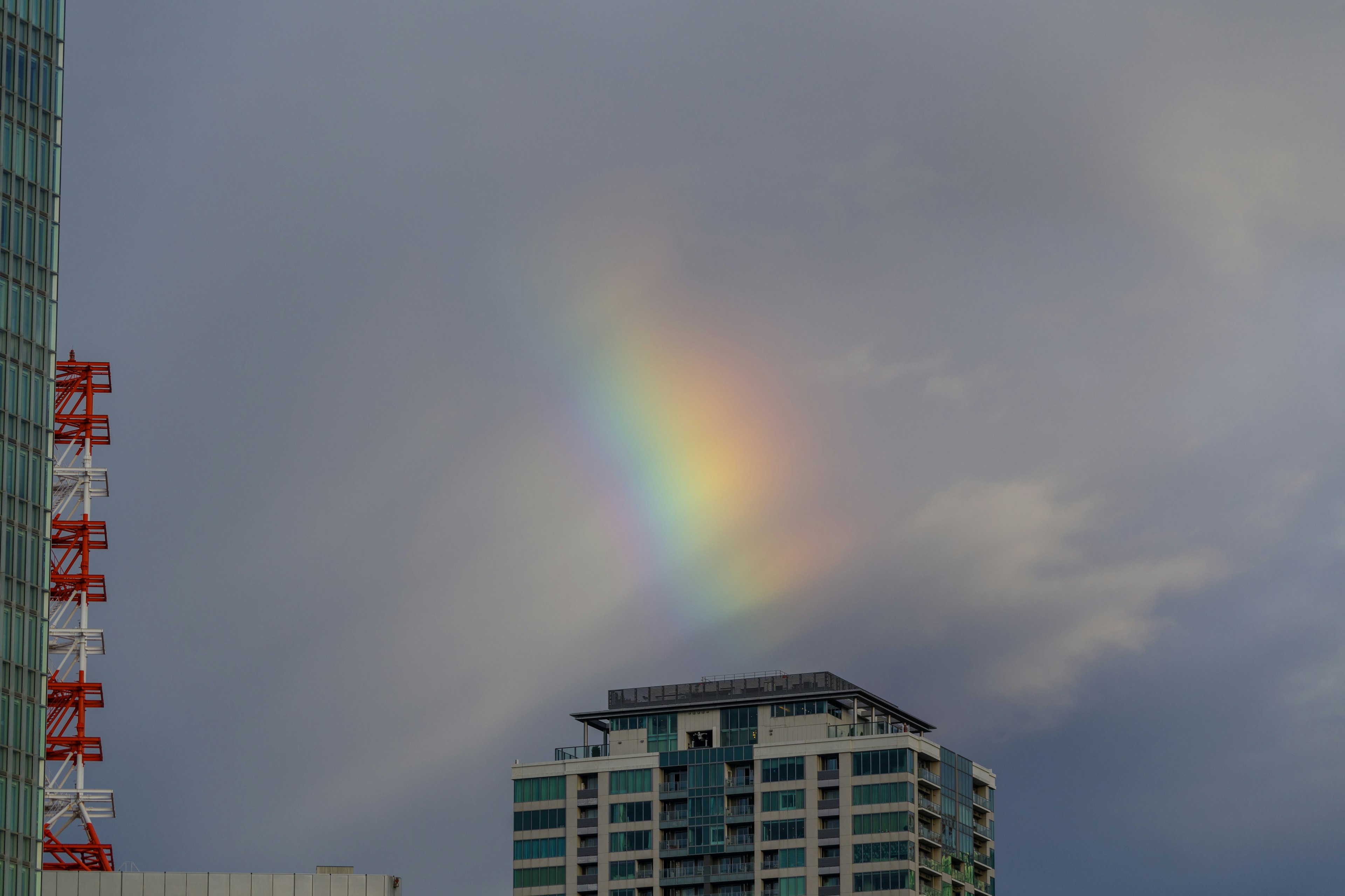 Rainbow appearing above a high-rise building under cloudy skies