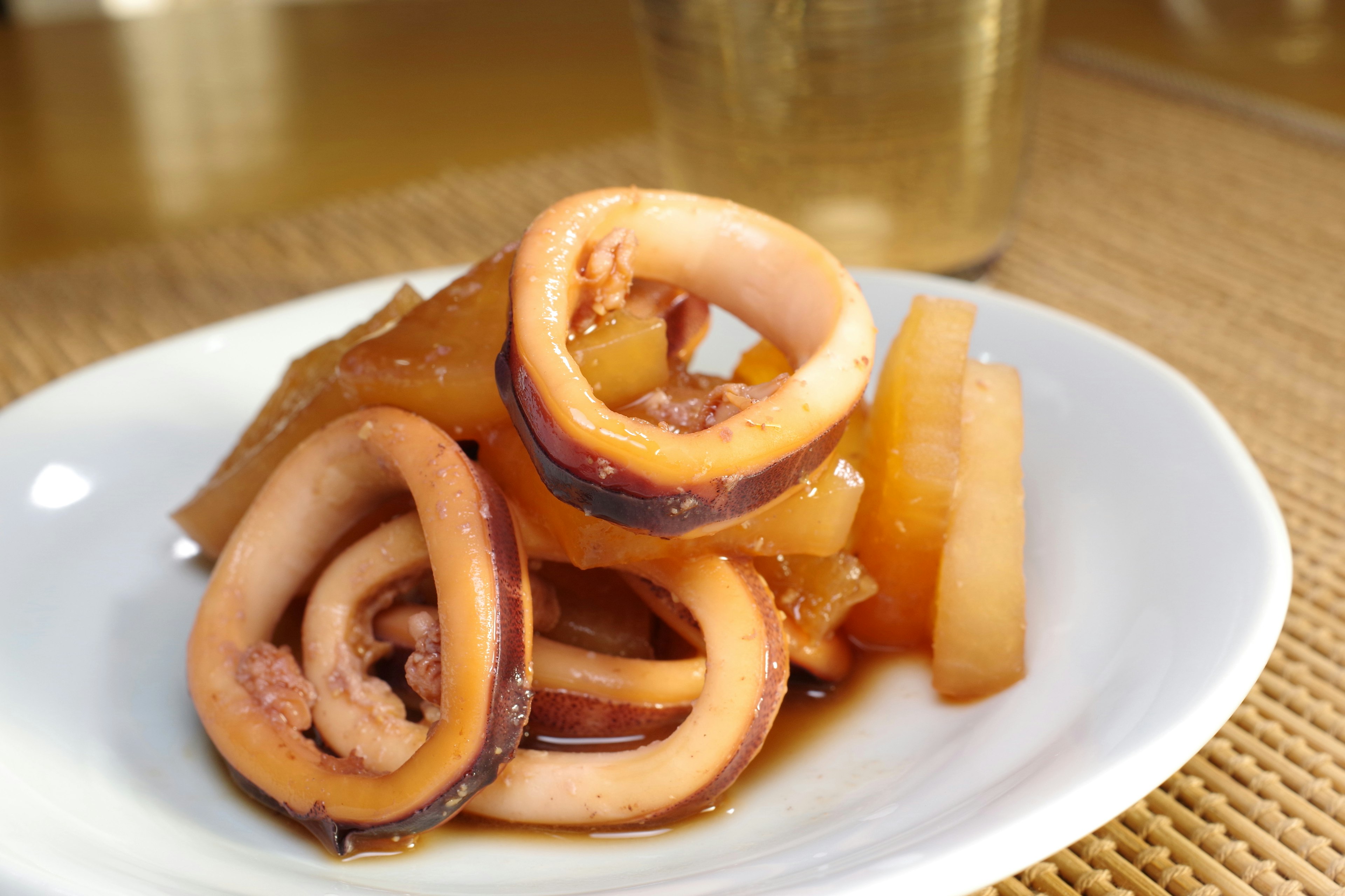 A plate of squid and daikon stew with a clear glass in the background