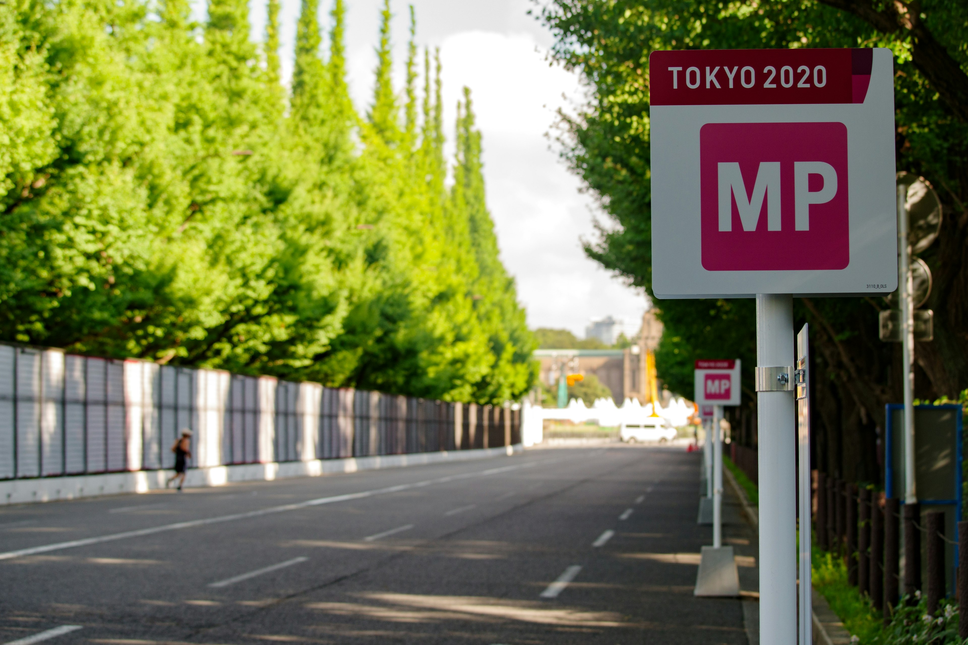 東京2020のバス停の看板と緑の木々が並ぶ通り