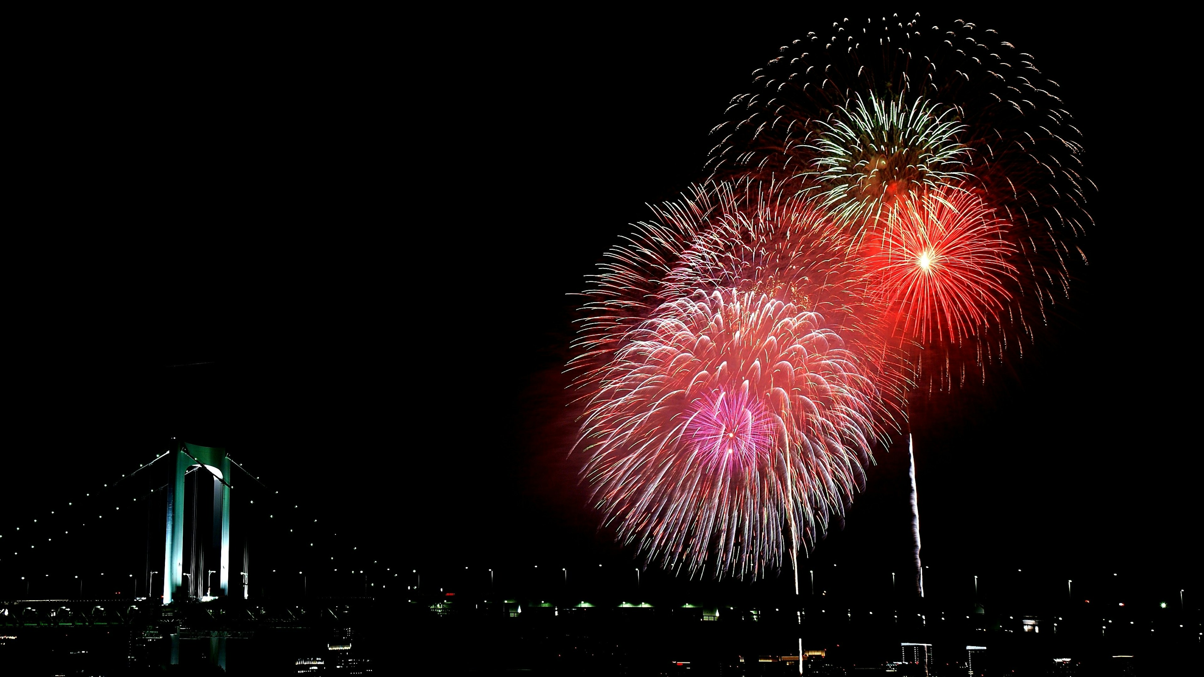 Fuegos artificiales estallan en el cielo nocturno con el Puente Rainbow al fondo