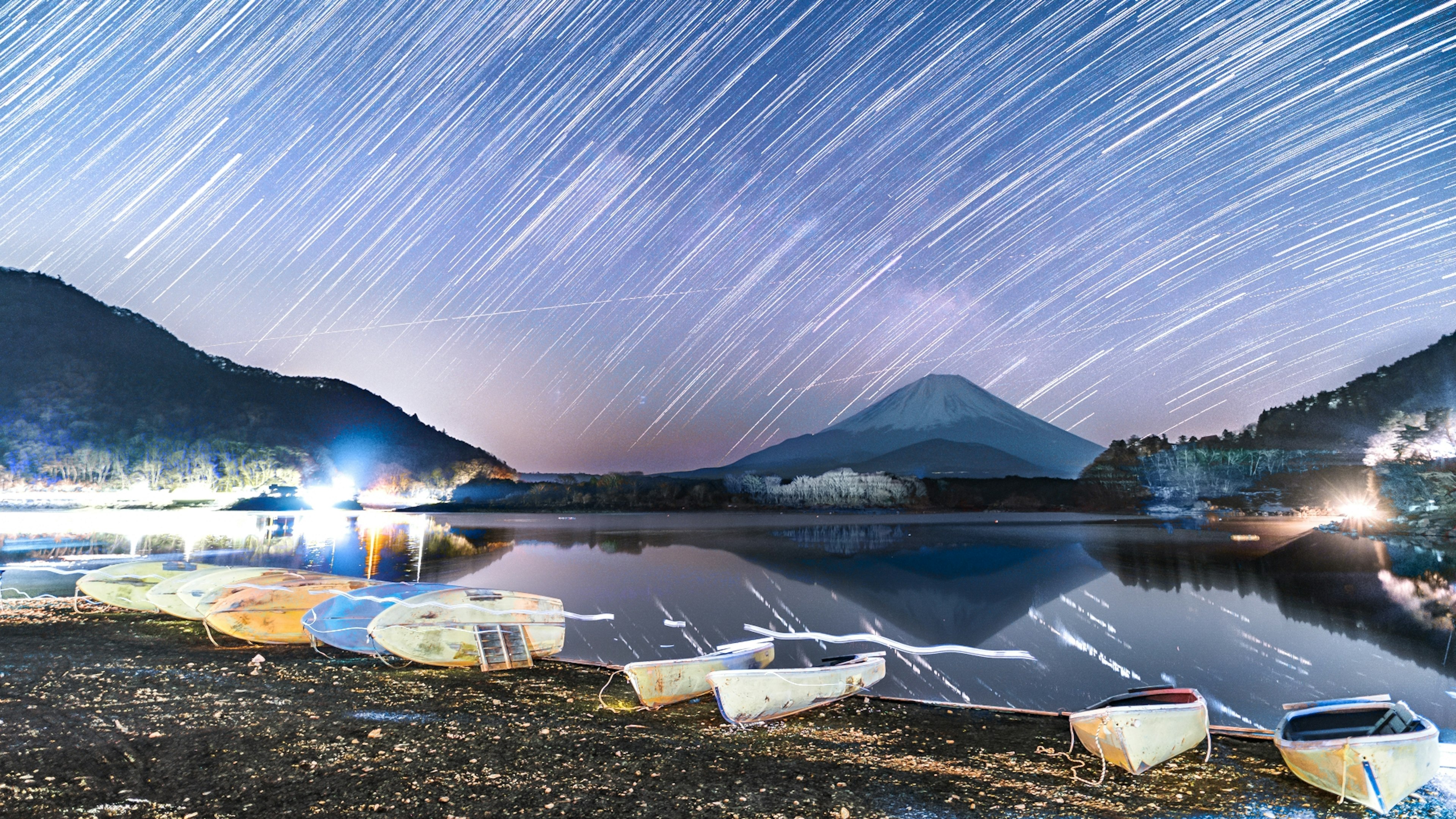 Traînées d'étoiles au-dessus du mont Fuji avec un lac serein et des bateaux au premier plan