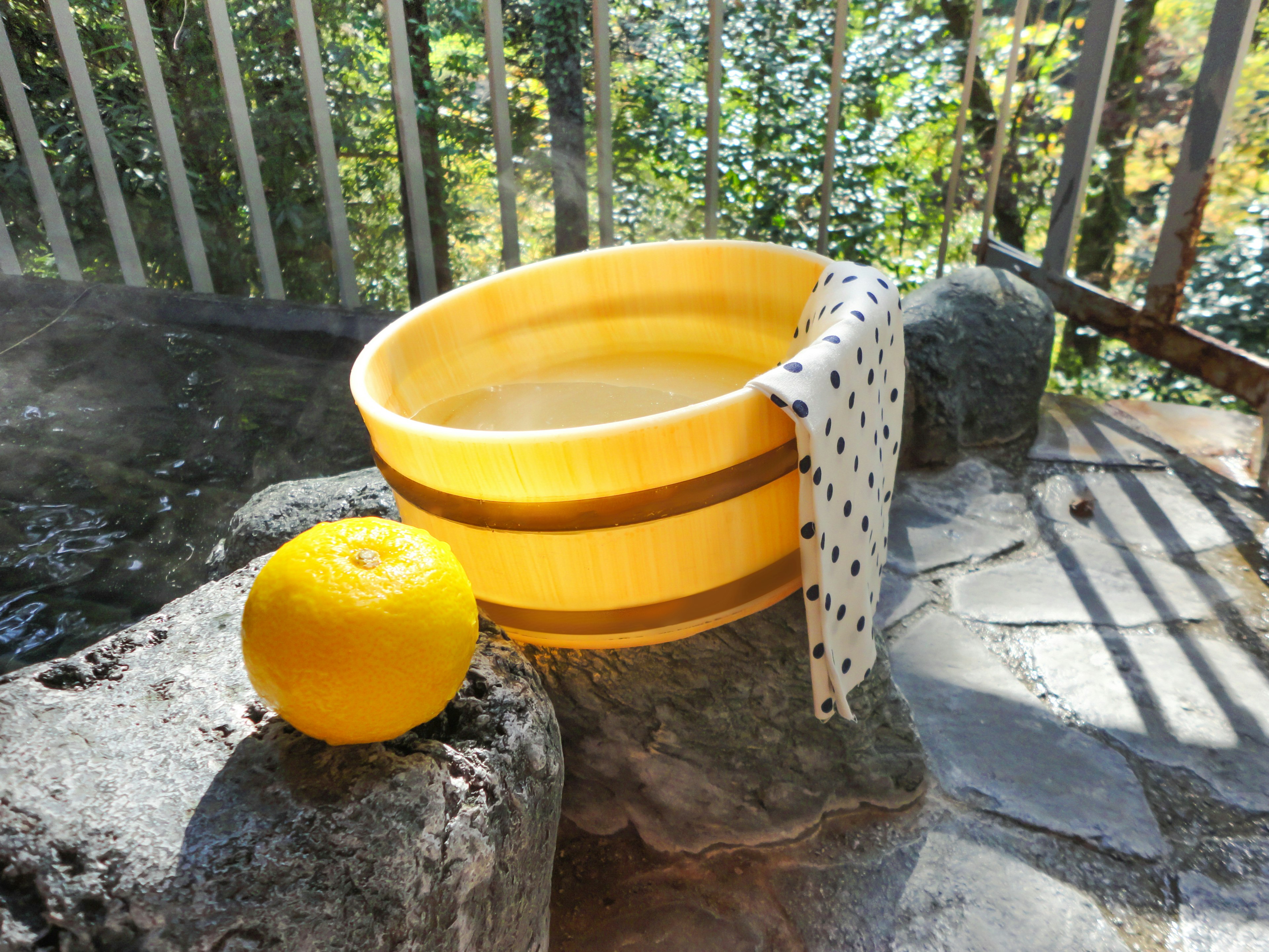 Bak kuning dengan buah jeruk di sampingnya di atas permukaan batu