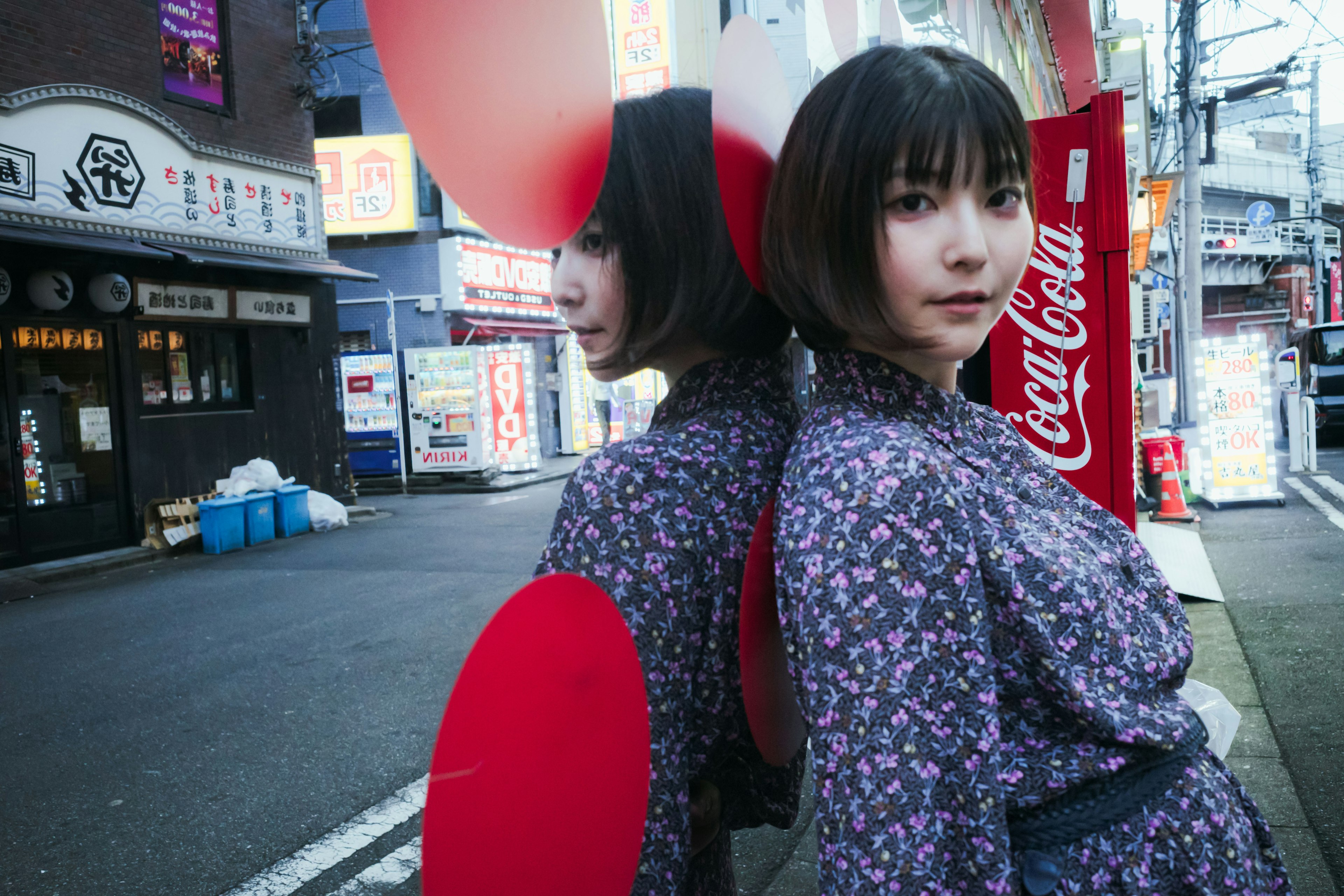 A woman in a floral dress standing back-to-back with her reflection against a red circle and Coca-Cola sign