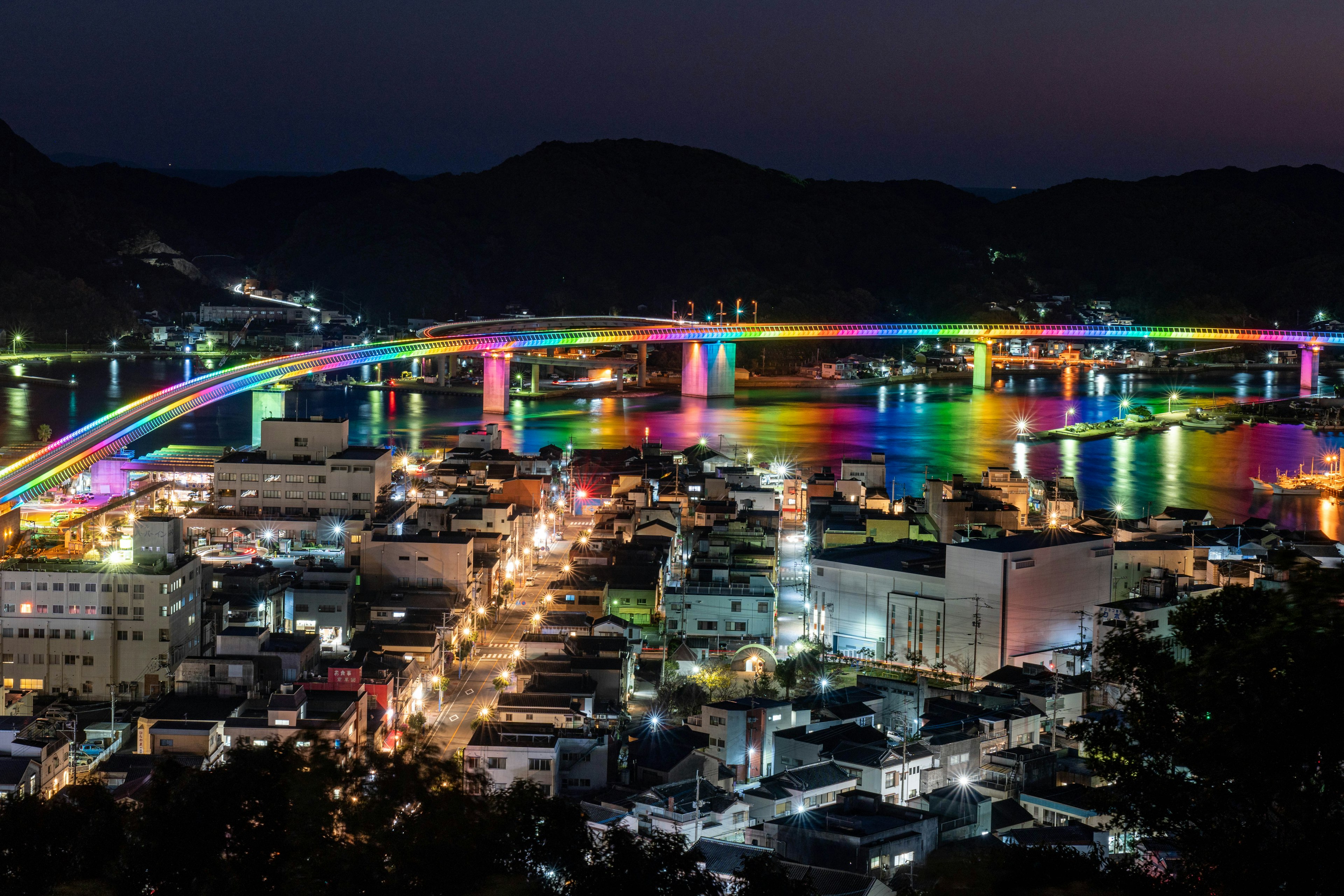 Vibrant night view of a city with a rainbow bridge and illuminated buildings