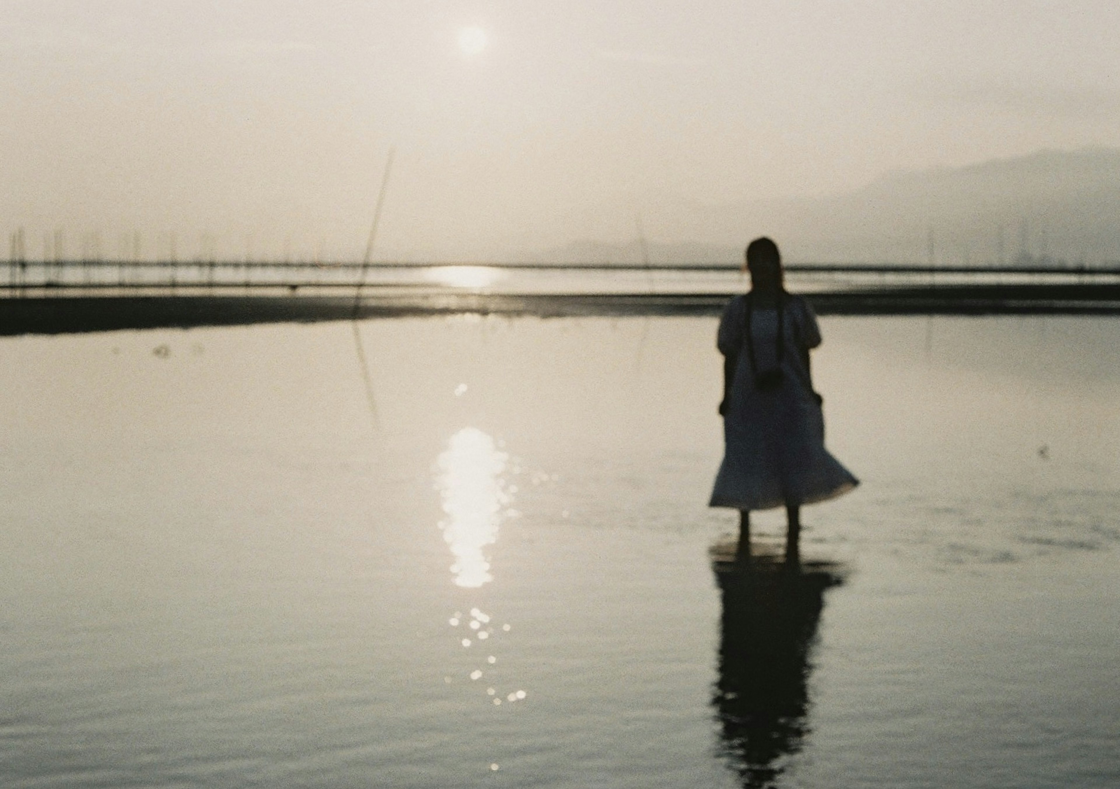 Silhouette einer Frau, die am Wasser steht mit Sonnenuntergangsreflexion