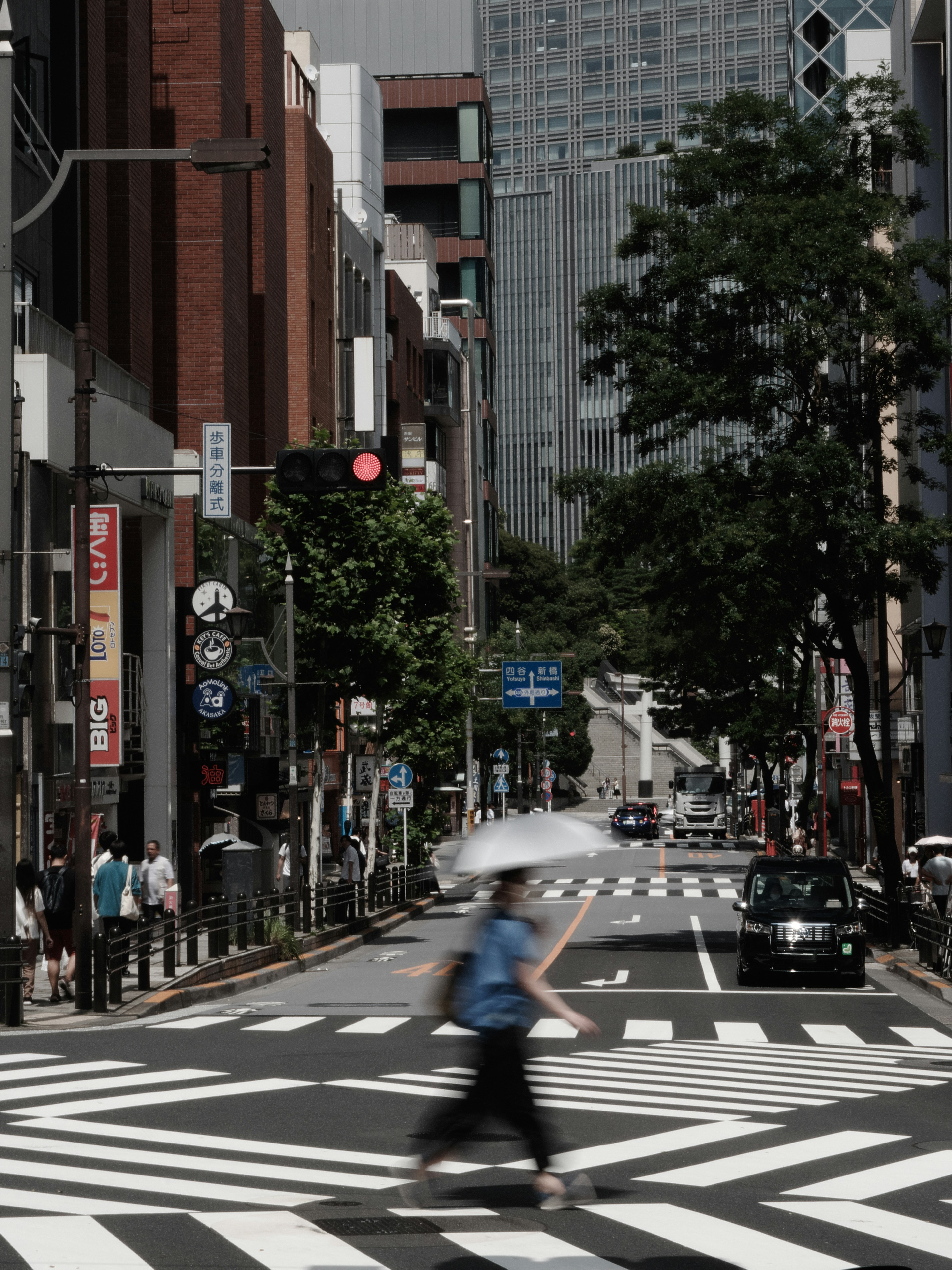 A person with an umbrella crossing a busy crosswalk surrounded by buildings