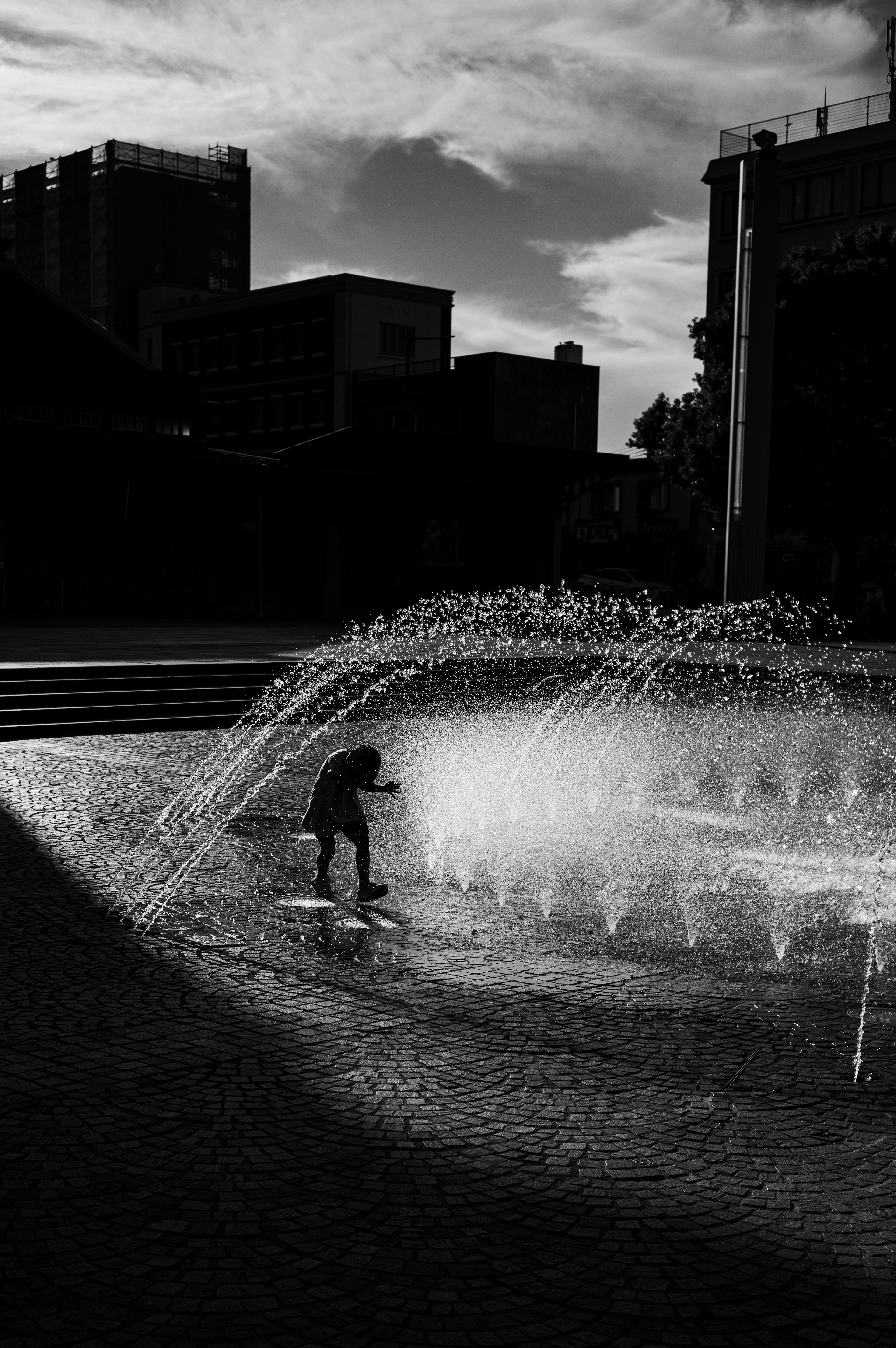 Silhouette di un bambino che gioca in una fontana d'acqua su sfondo scuro