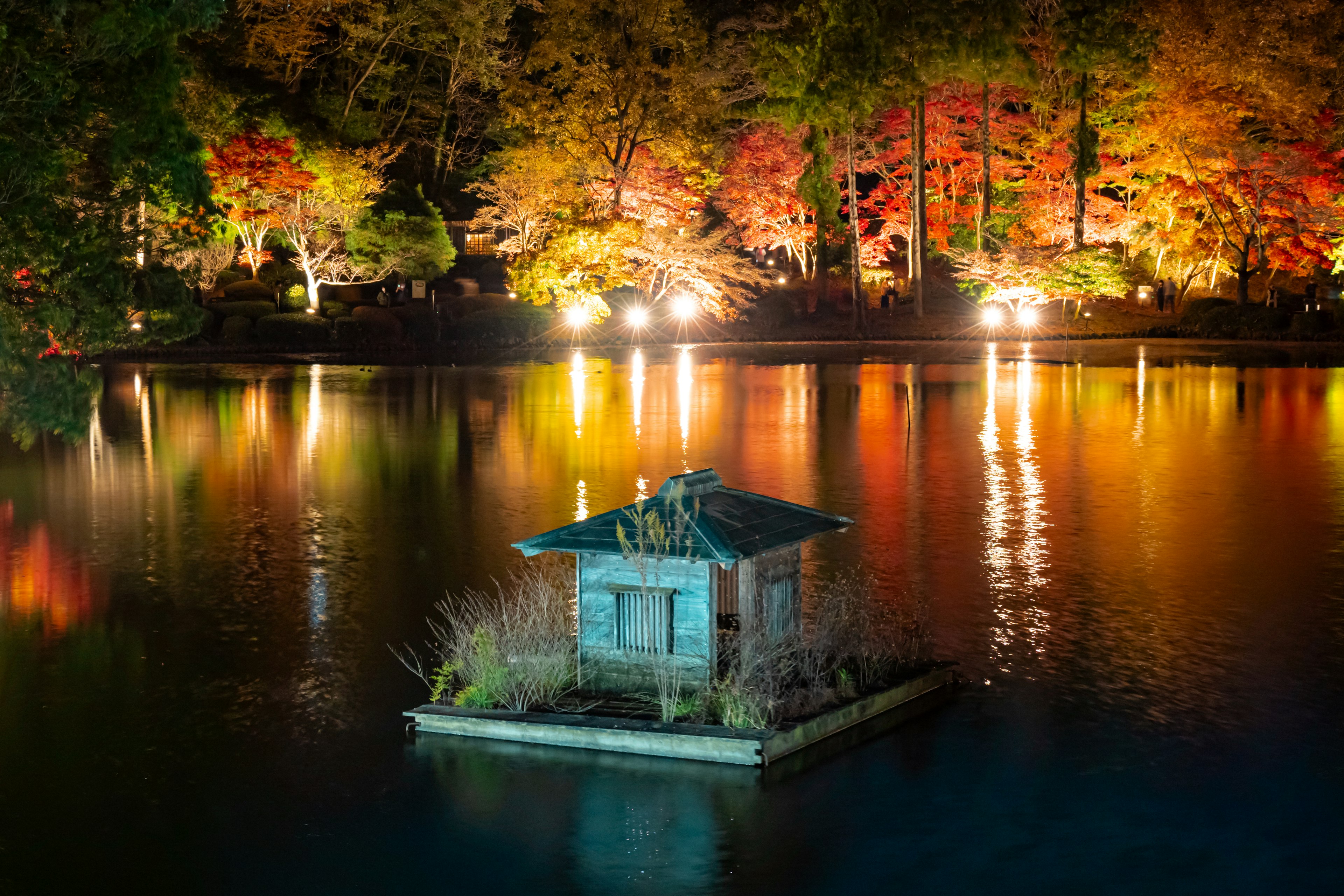 Une petite structure flottant sur un lac entouré de feuillage d'automne coloré la nuit