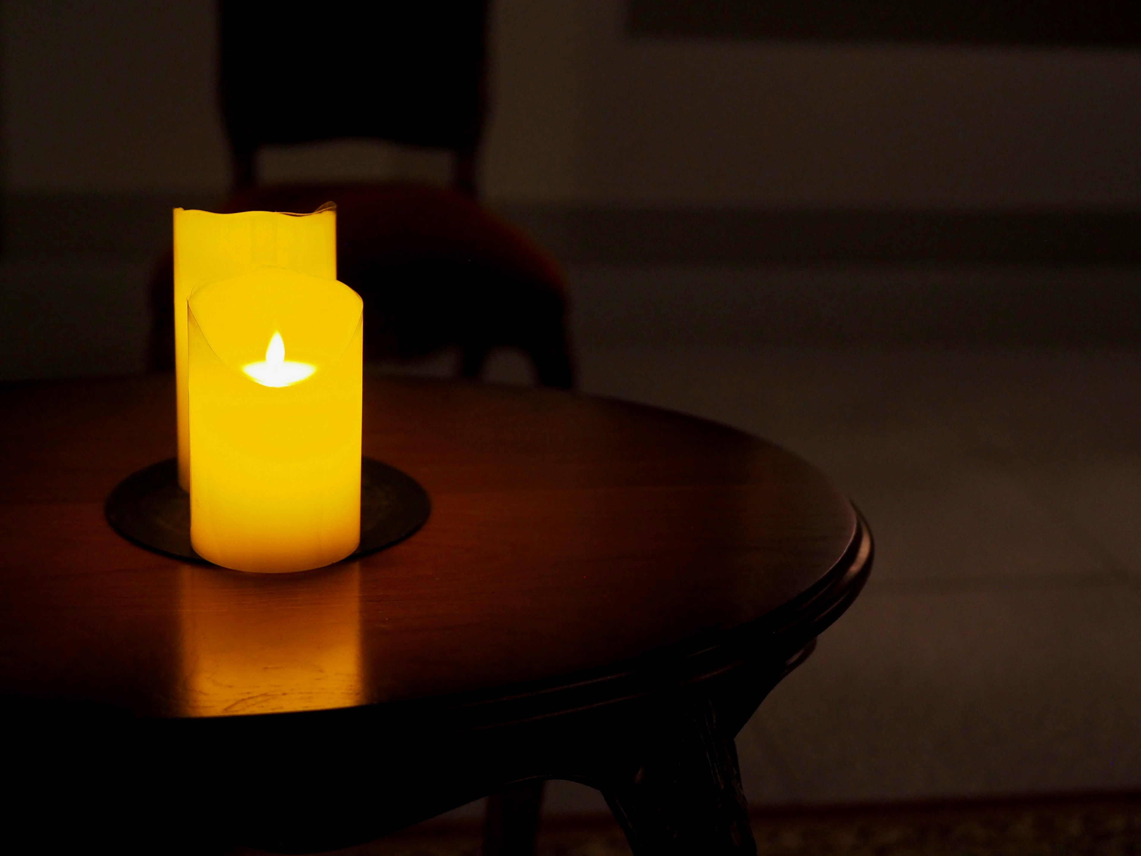 Glowing yellow candle on a wooden table in a dimly lit room