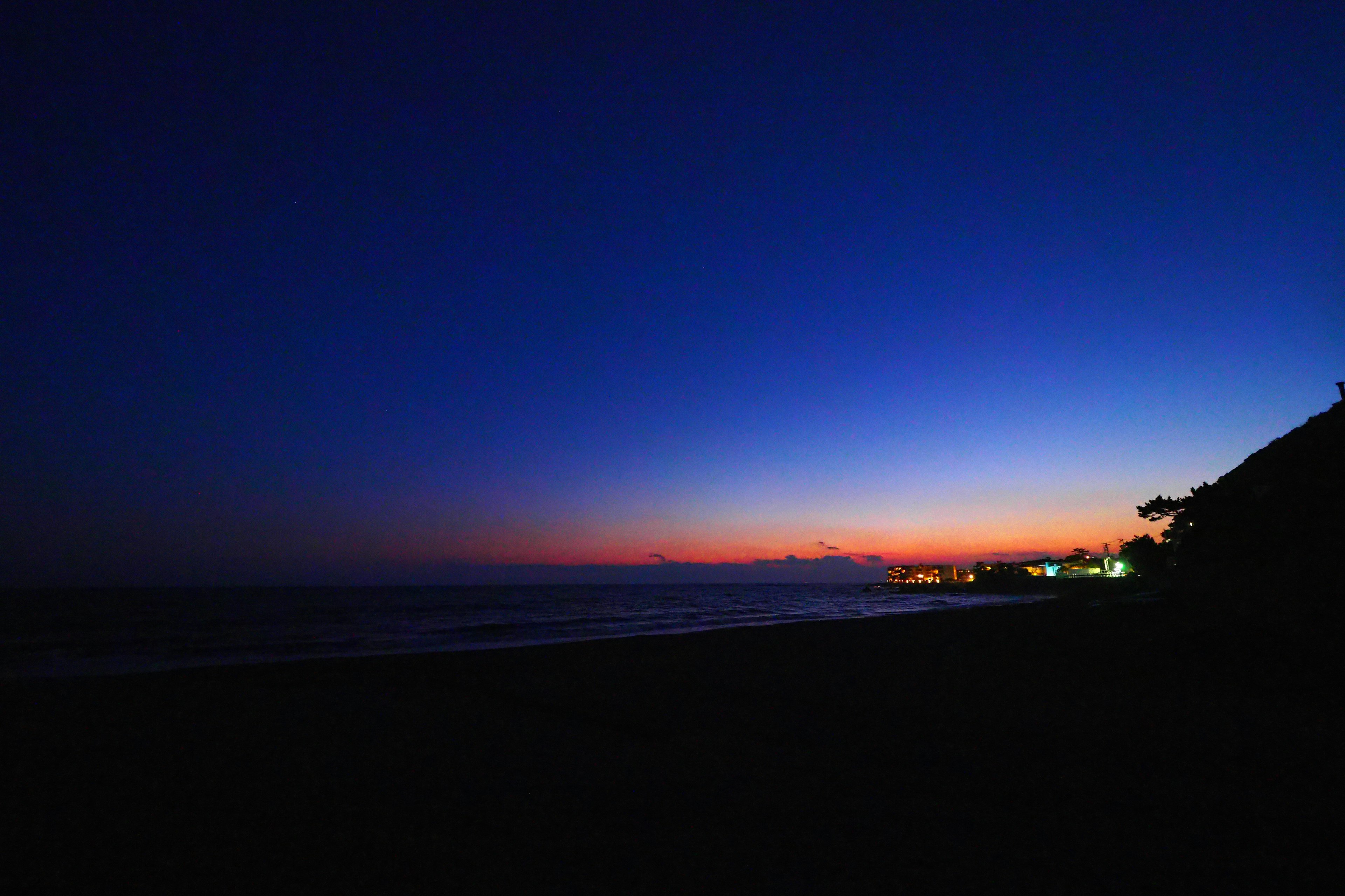 美しい海の夕暮れ時の風景、深い青とオレンジのグラデーション、遠くの灯りが見える