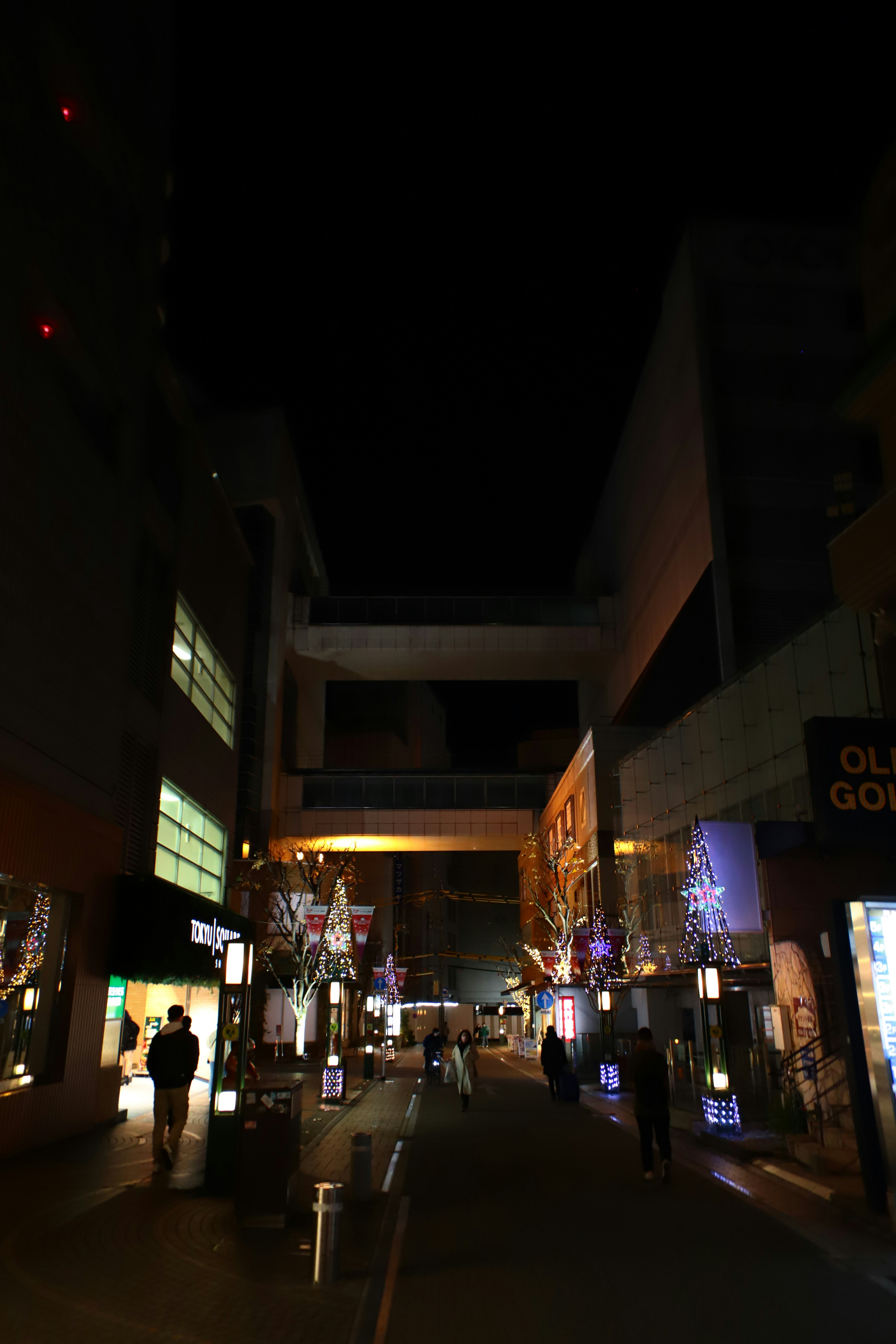 Illuminated street scene at night with silhouettes of people