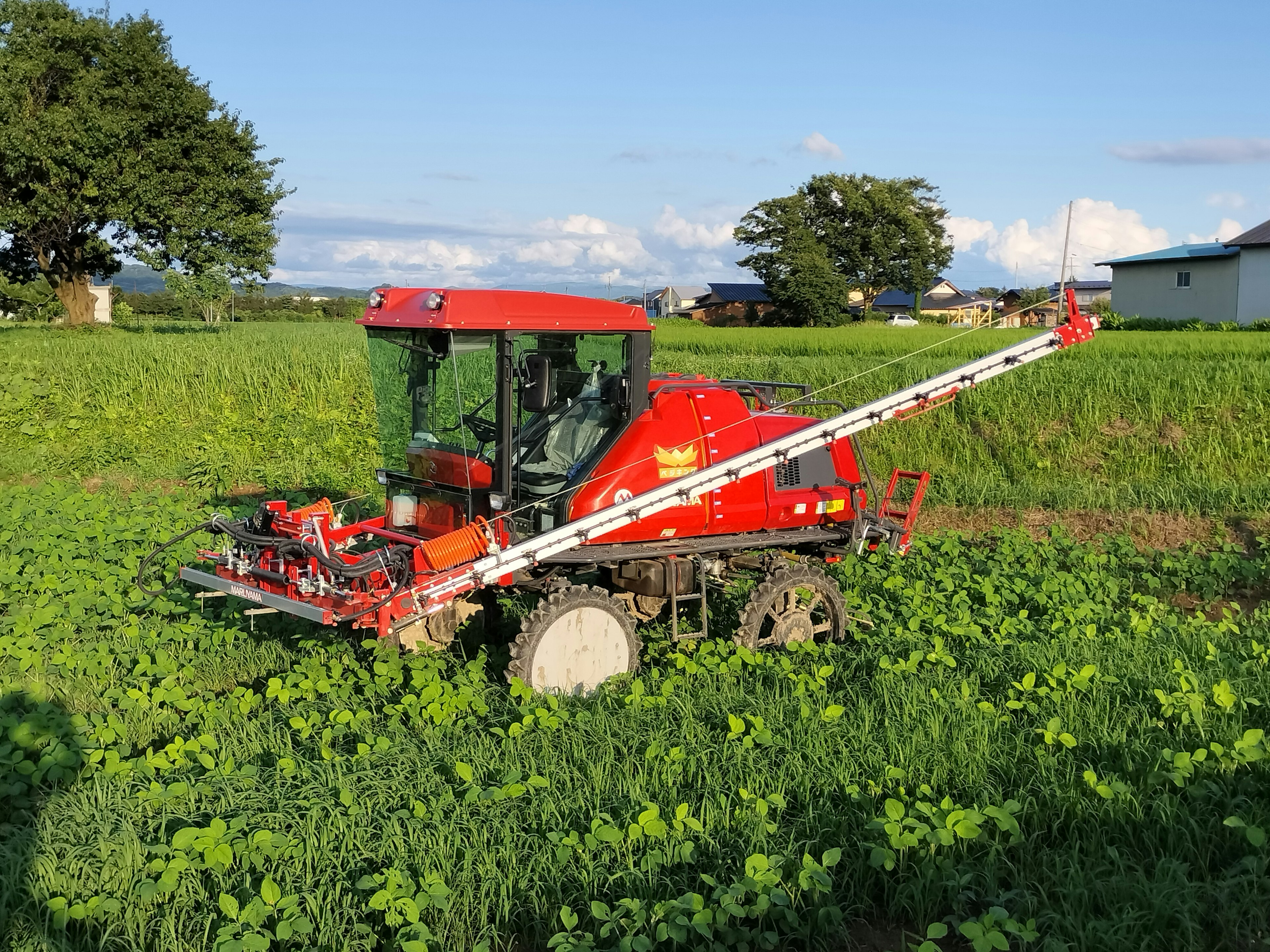 赤い農機具が緑の作物の中で作業している風景