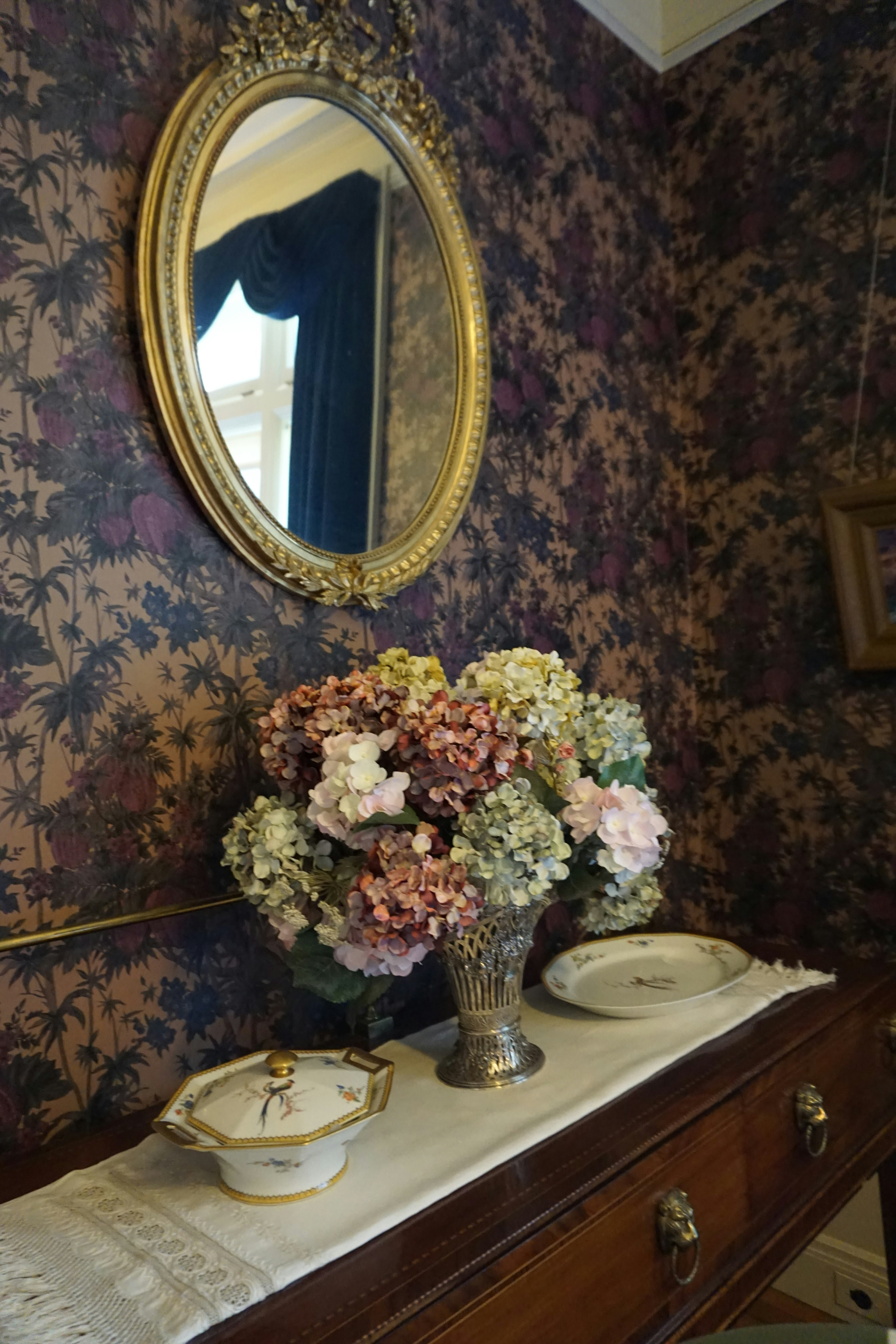 Una esquina de una habitación con un jarrón de flores coloridas y un espejo