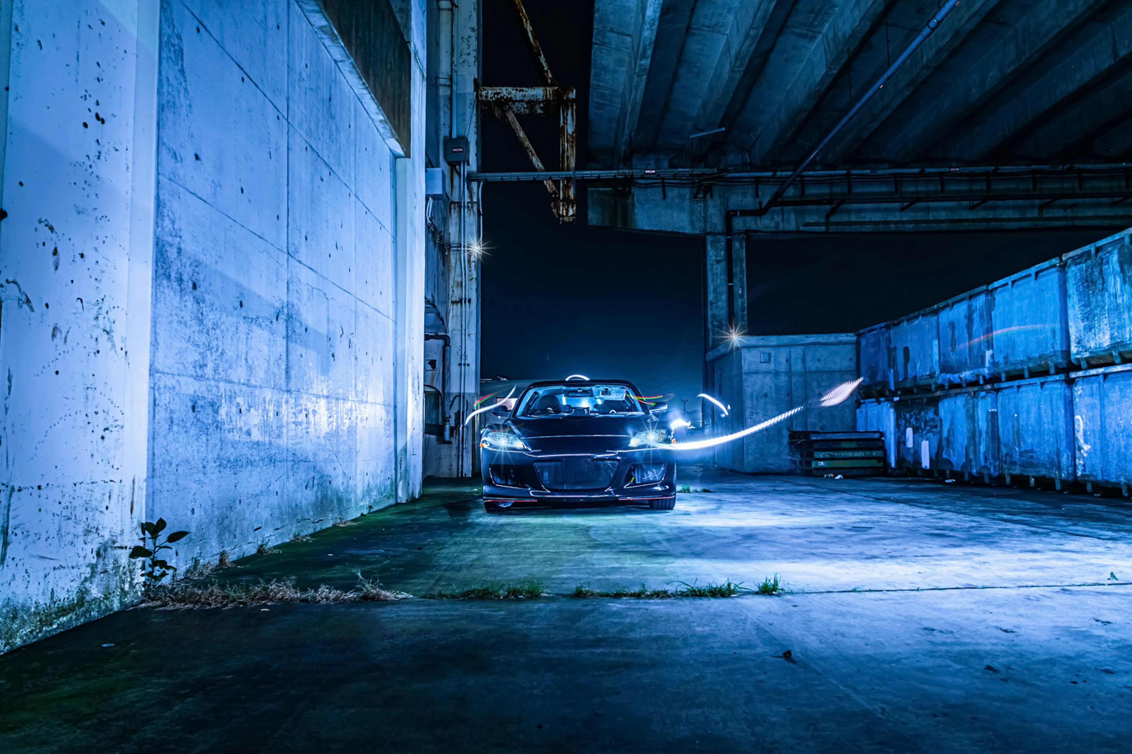 Un coche iluminado por luz azul en un entorno industrial abandonado