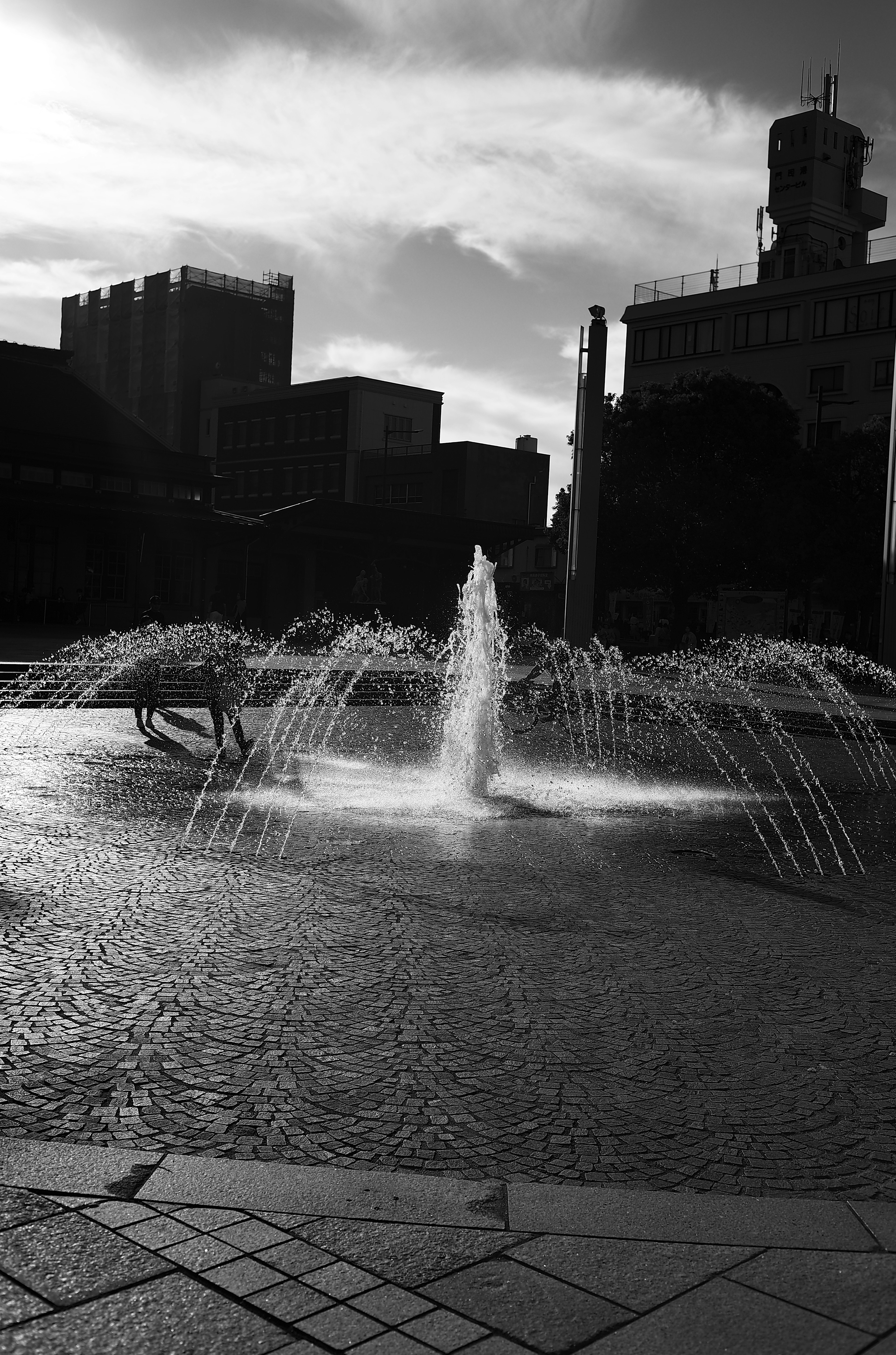 Fontaine en noir et blanc au centre avec des bâtiments en silhouette en arrière-plan