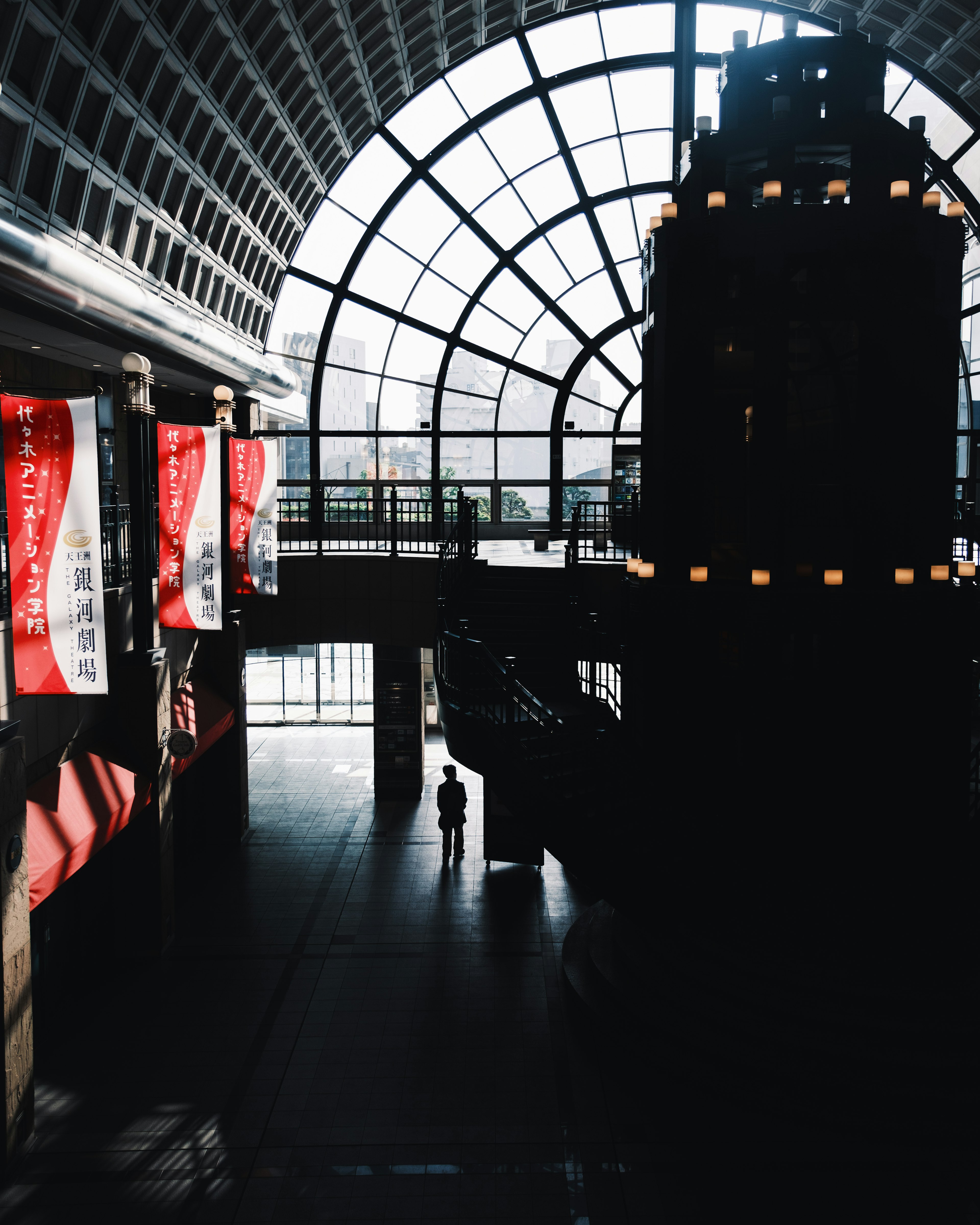 Interior de un gran edificio con un techo de vidrio mostrando la silueta de una persona y banderas rojas