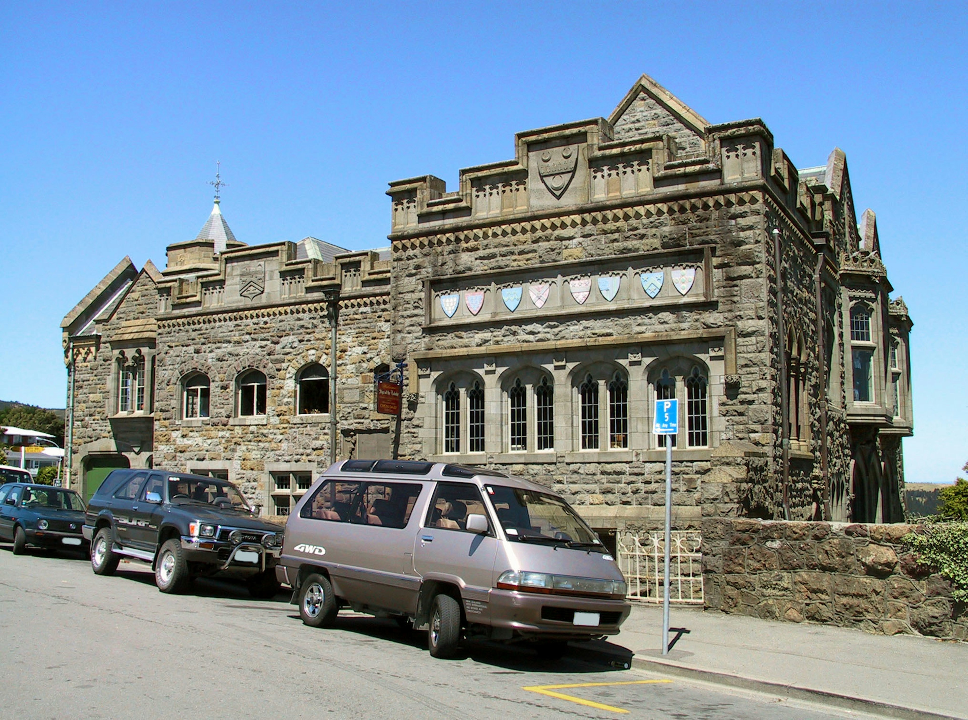 Edificio de piedra con elementos decorativos junto a vehículos estacionados y cielo azul claro