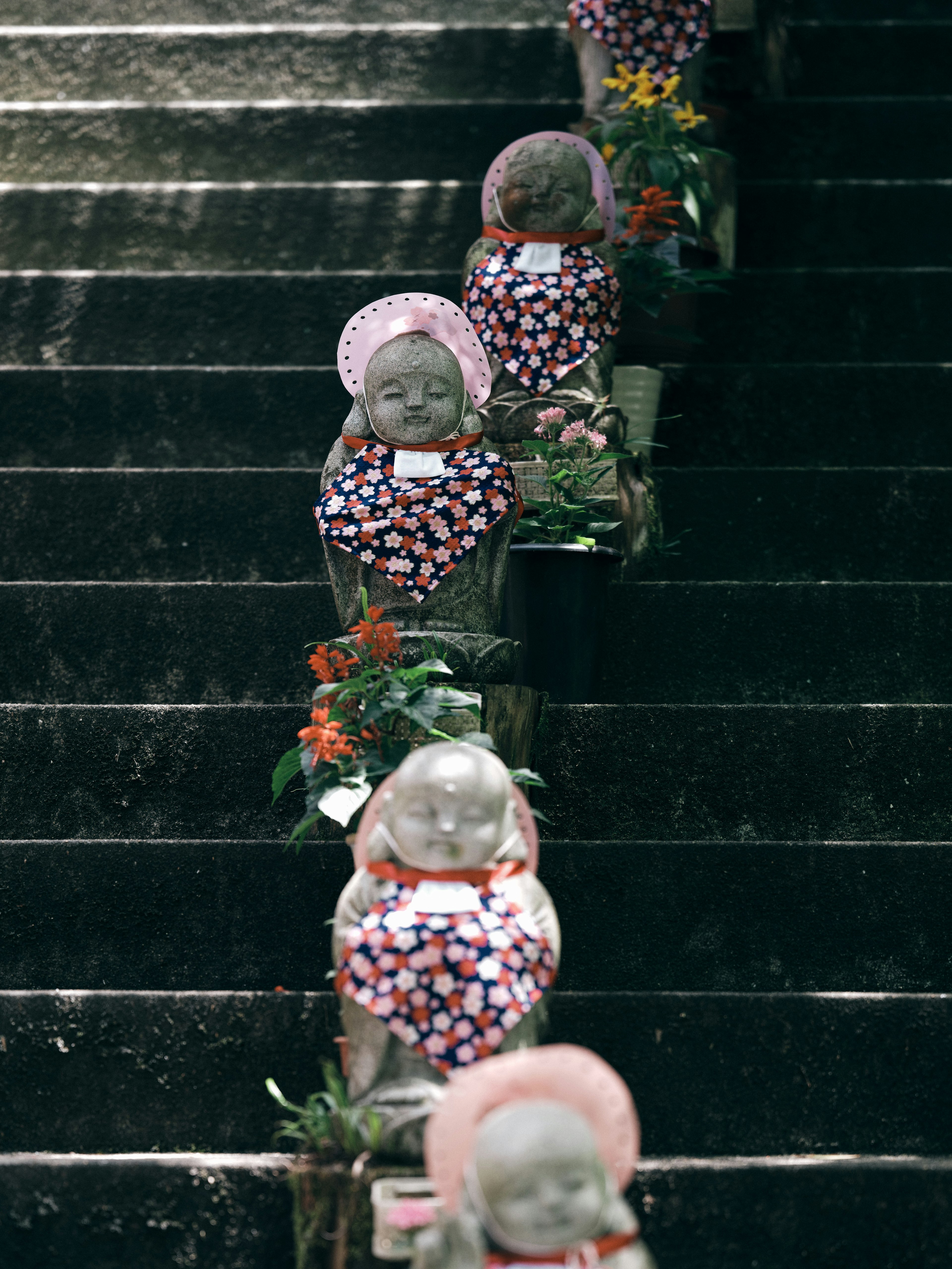 Cute stone statues lined up on stairs surrounded by flowers and greenery