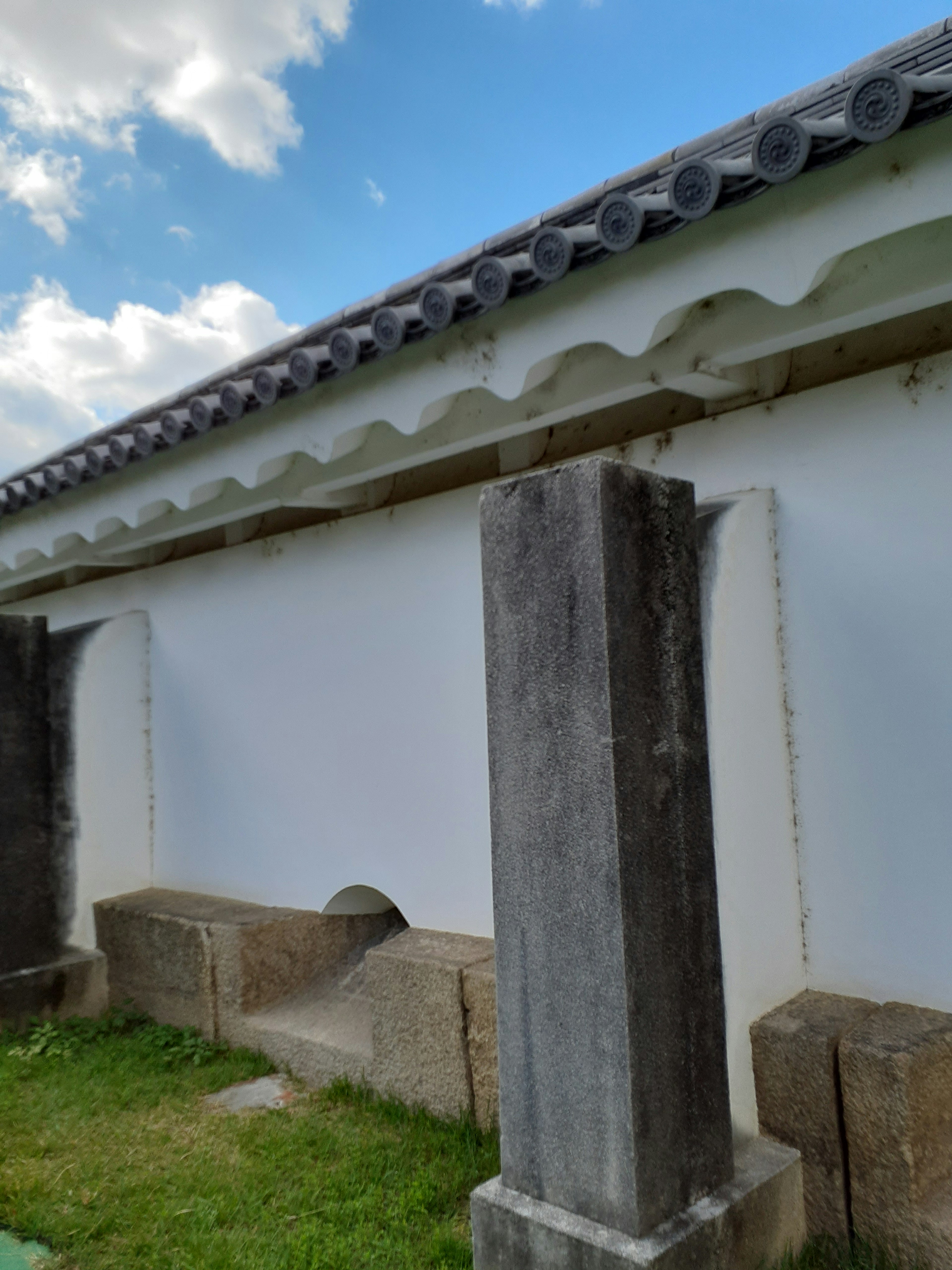 Side view of a traditional building featuring a white wall and stone pillars under a blue sky