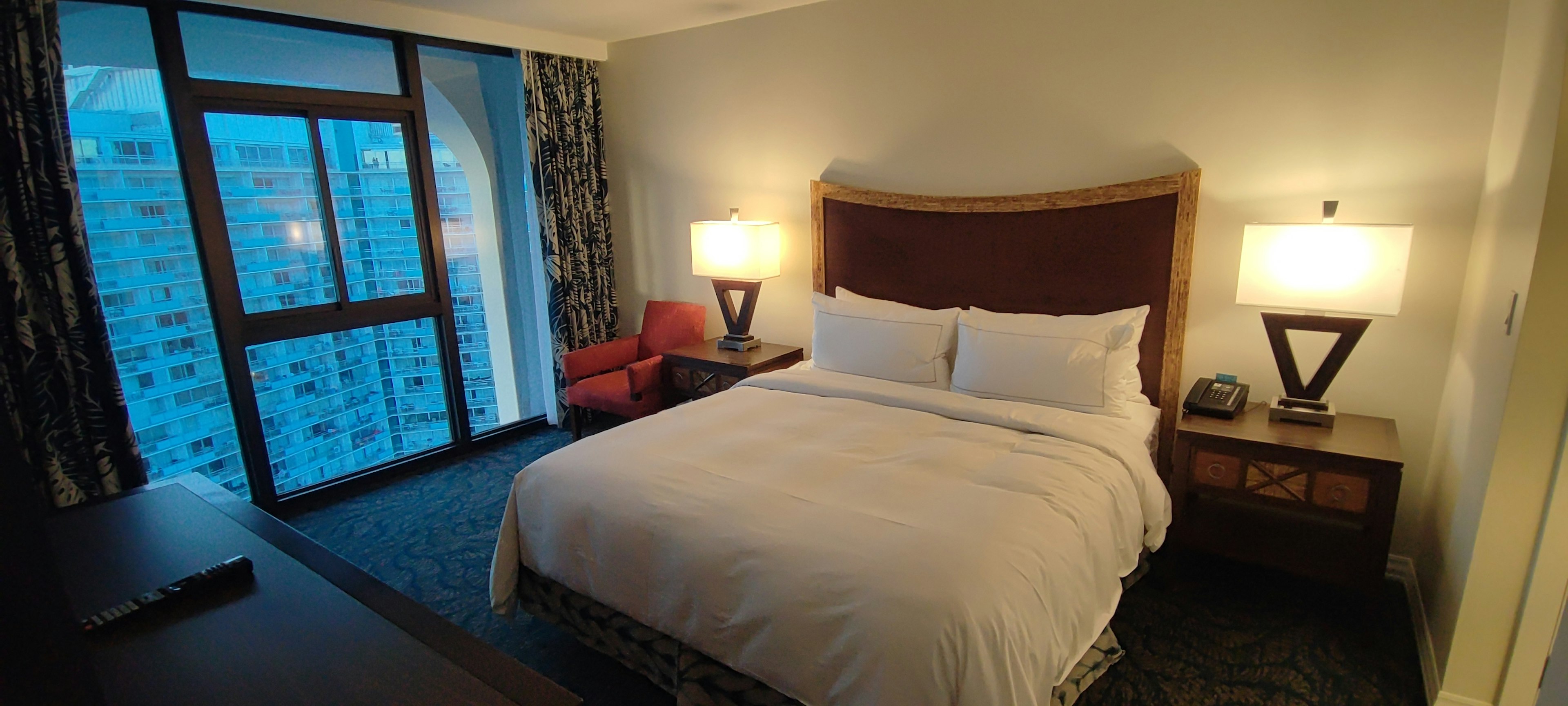 Cozy hotel room featuring a queen bed and large windows with blue light