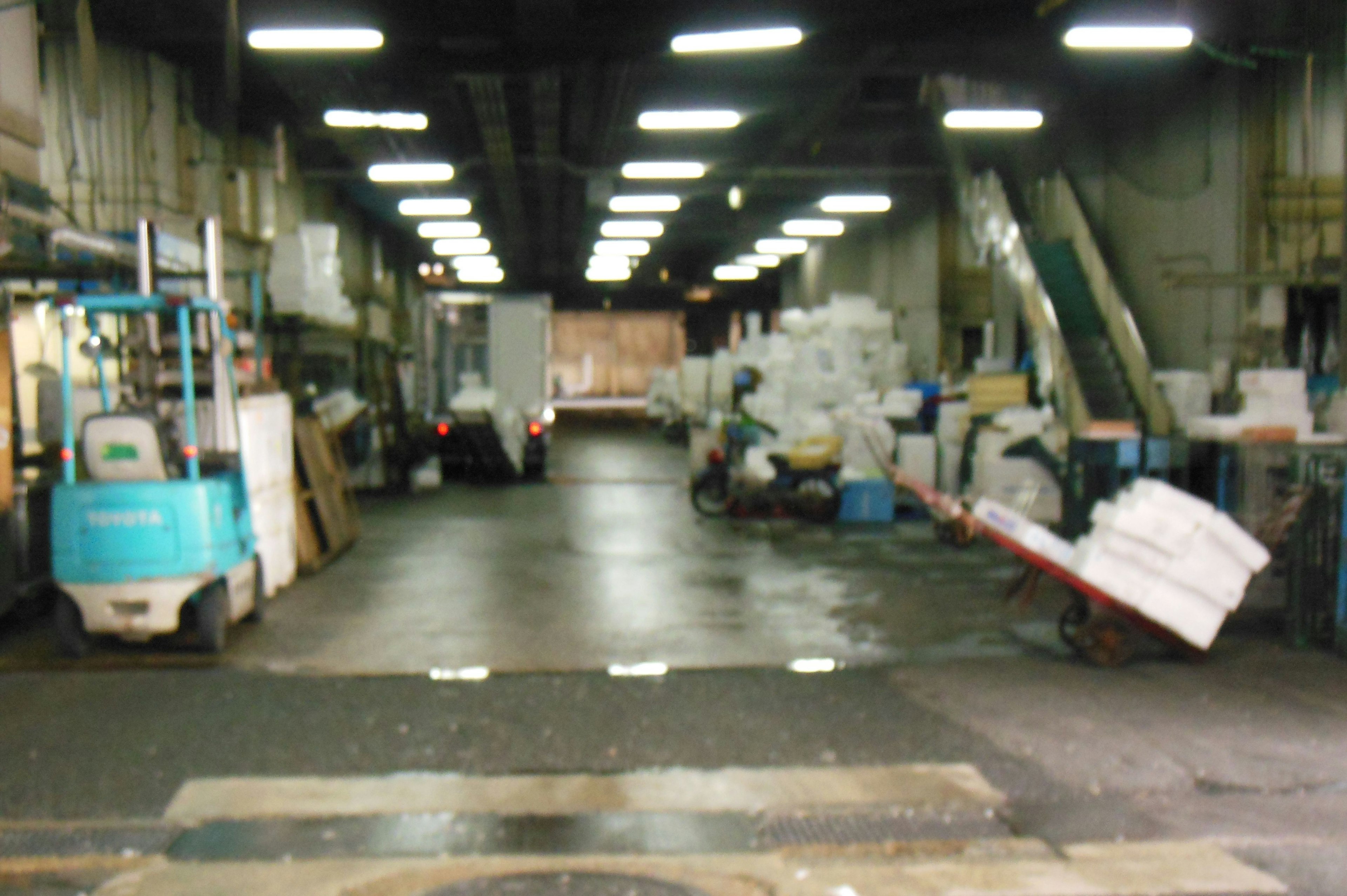 Interno di un magazzino poco illuminato con un carrello elevatore e un camion circondati da materiali impilati