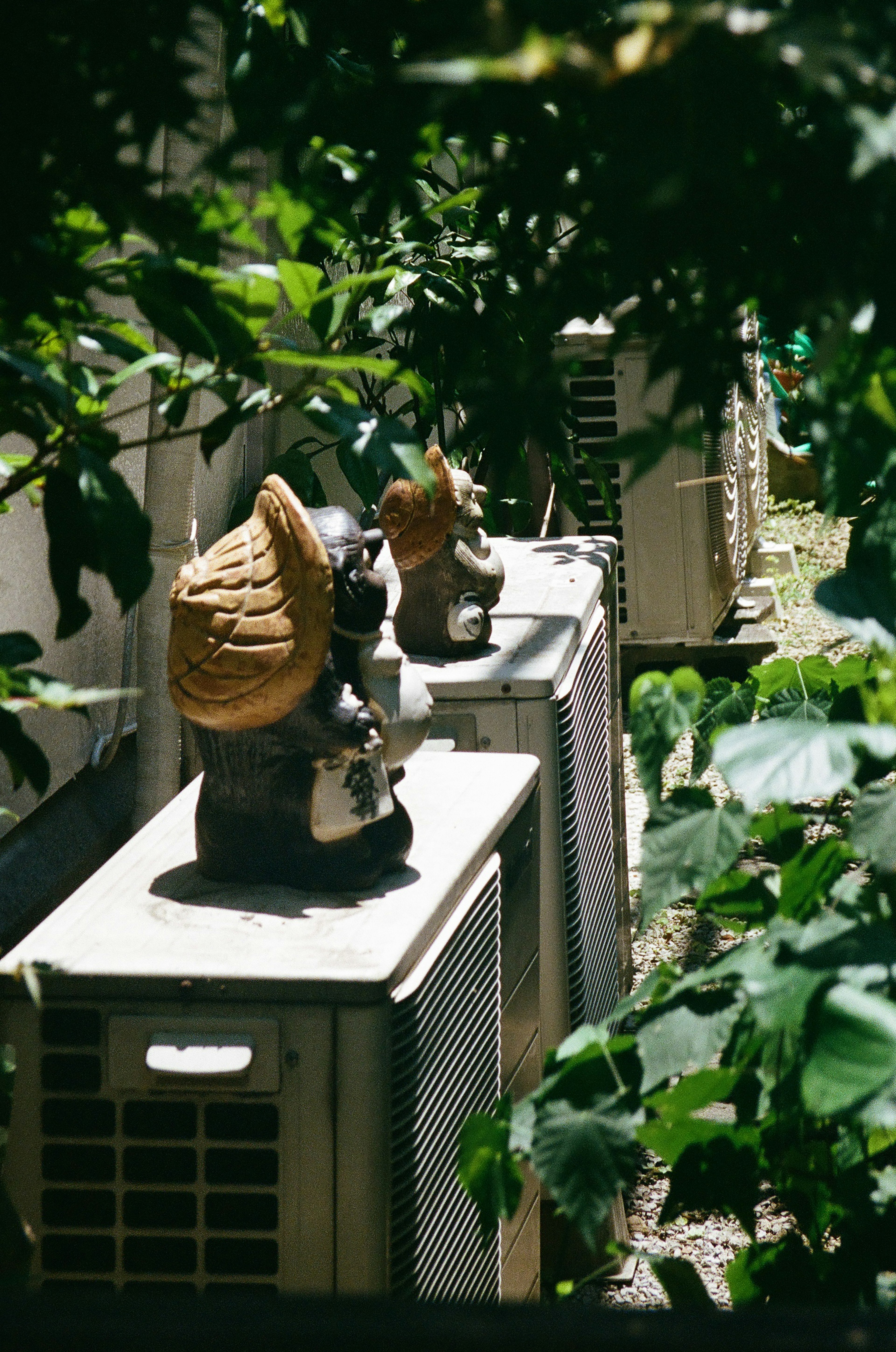 Estatuas decorativas sobre unidades de aire acondicionado rodeadas de vegetación