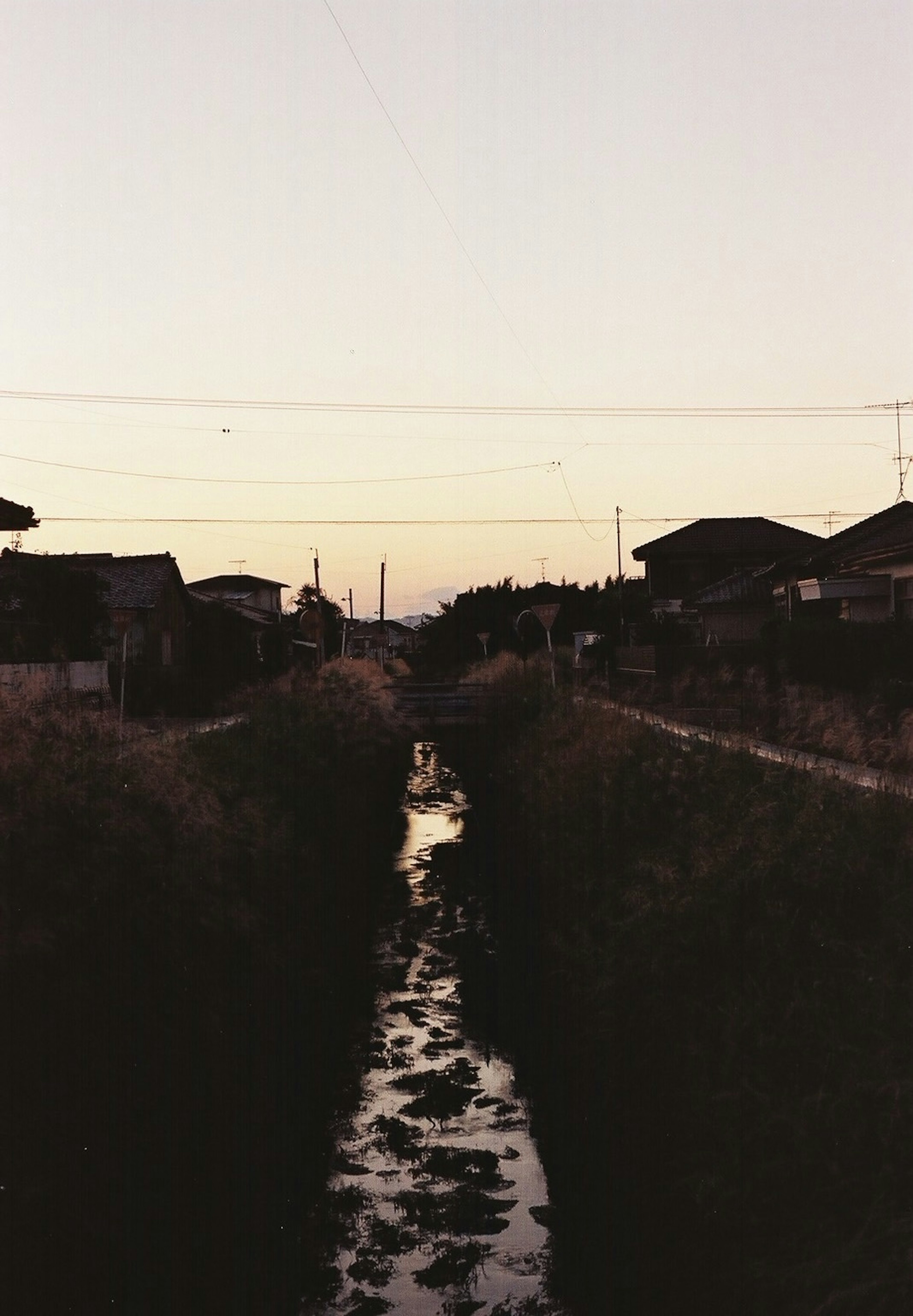 Twilight scene of a narrow stream with silhouettes of houses