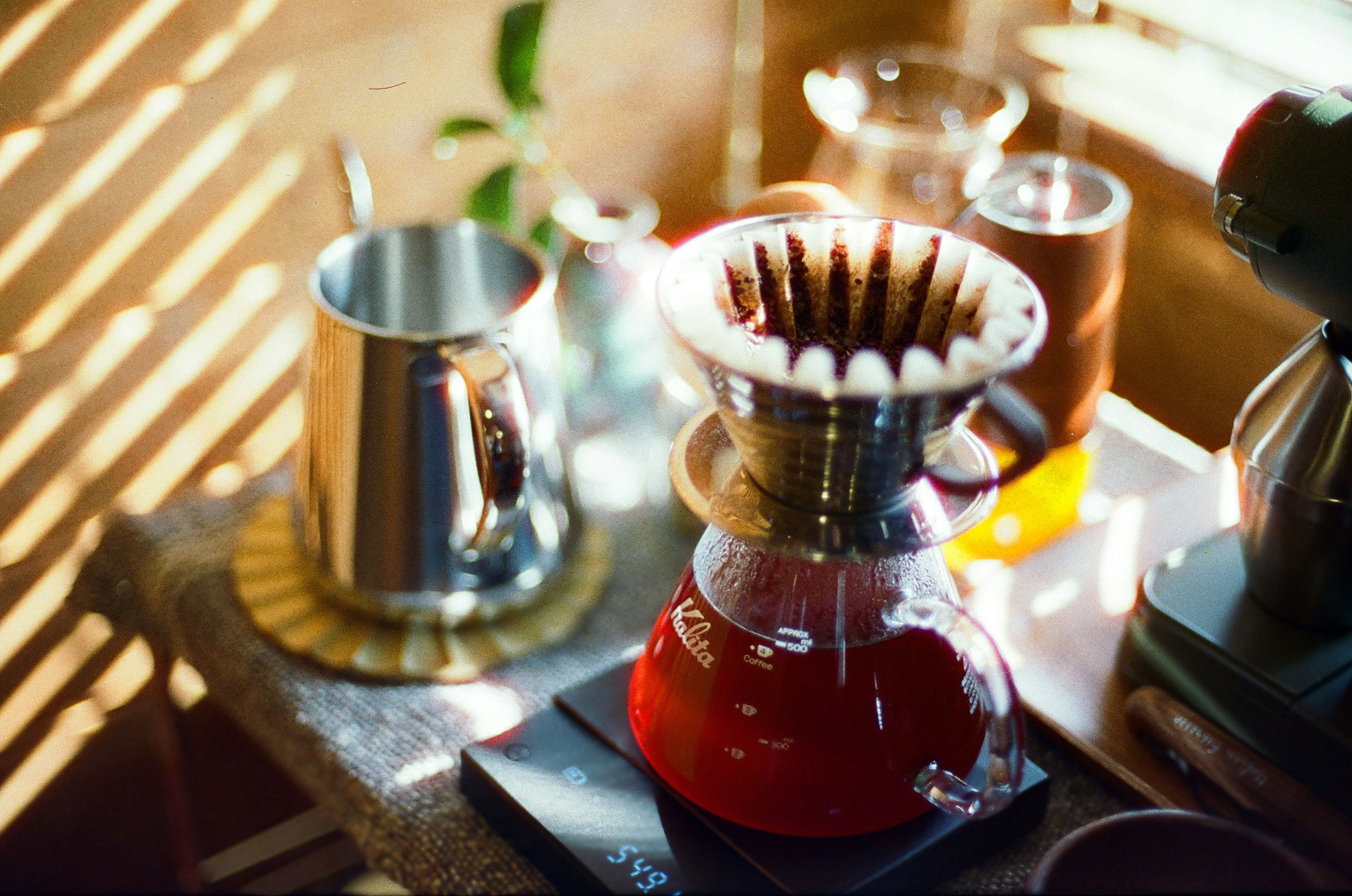 Red coffee dripper and silver kettle on a countertop with coffee tools