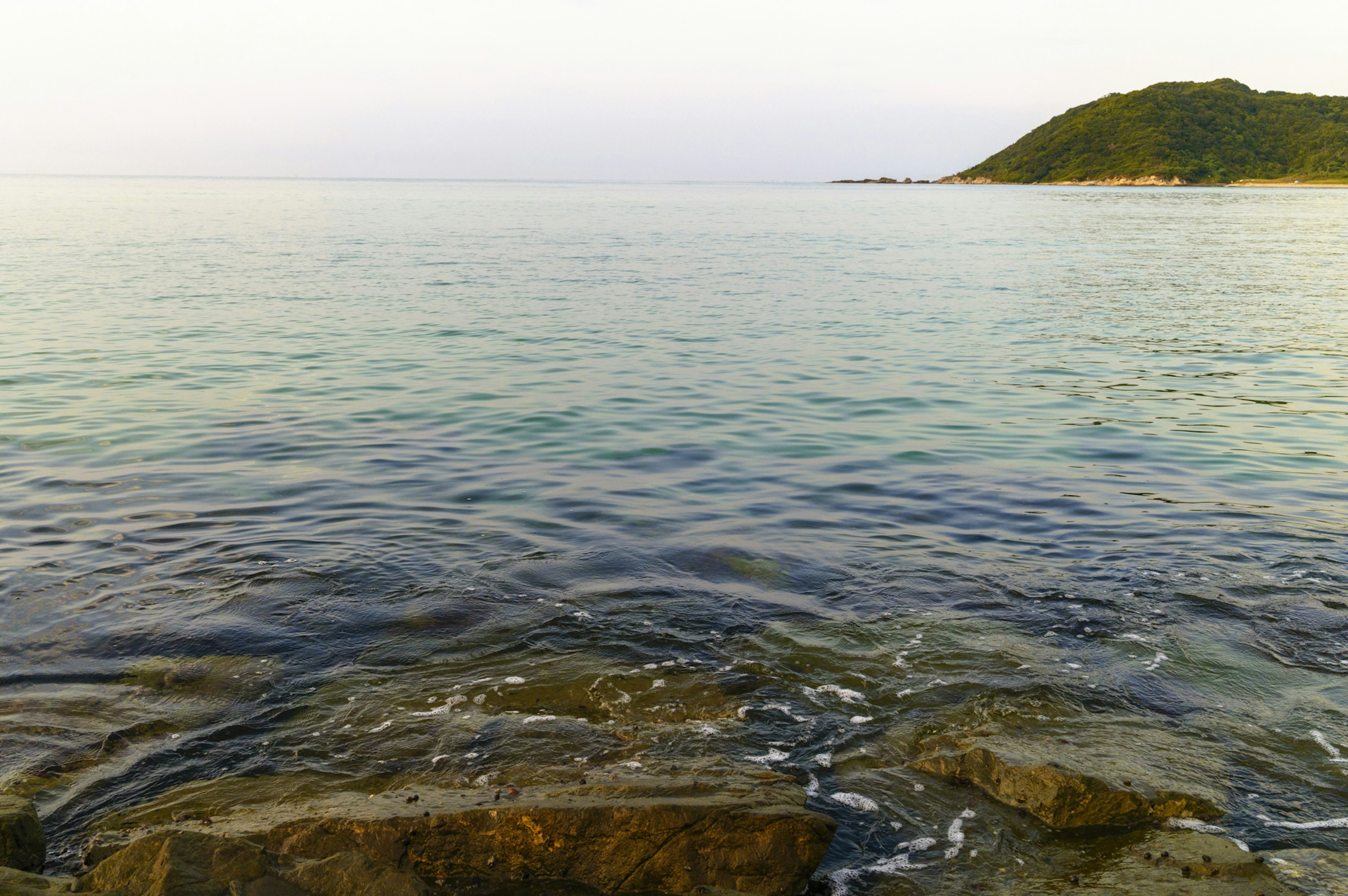 Mer calme avec des rochers et une colline au loin