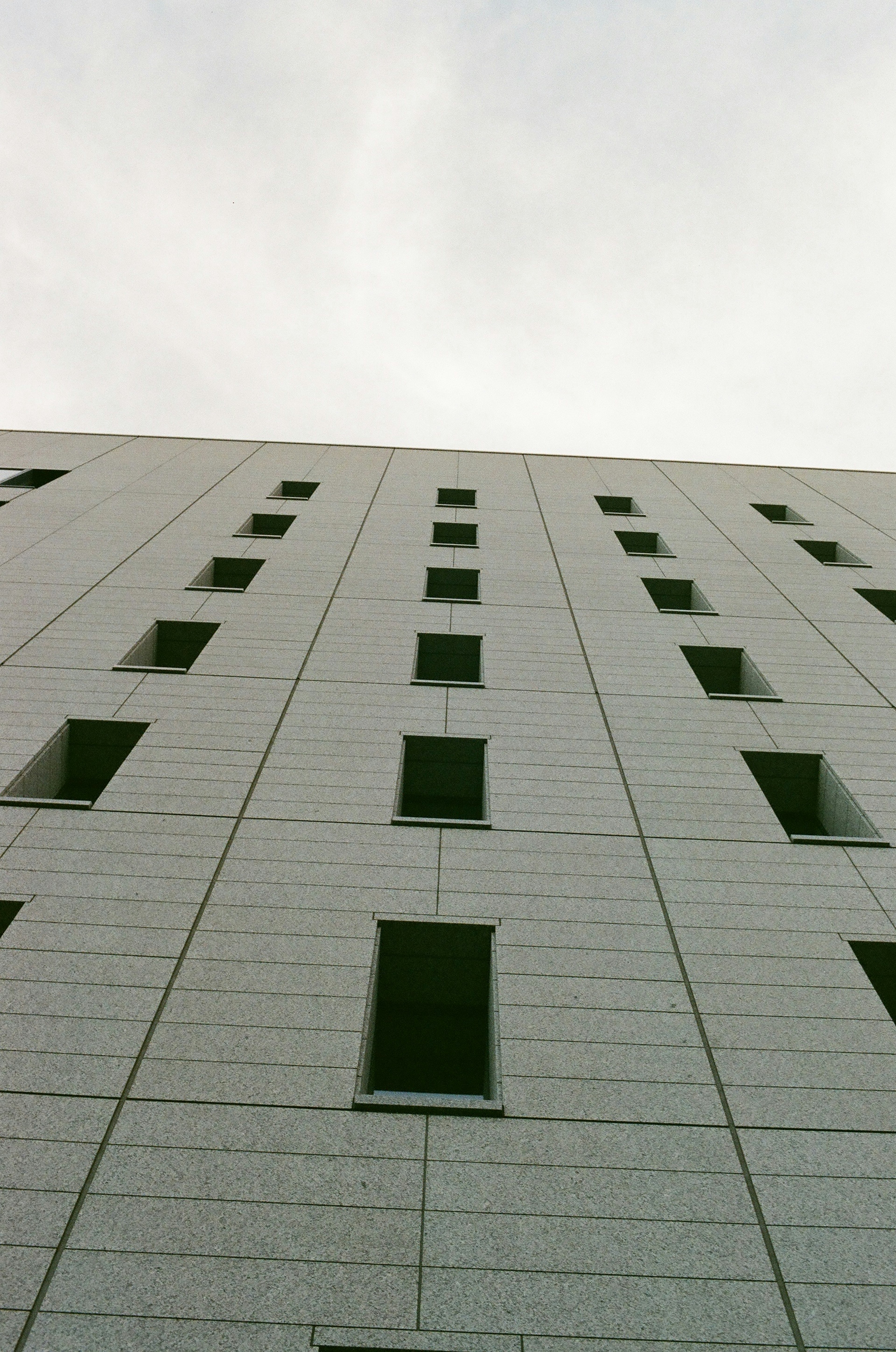 Facade of a high-rise building viewed from below with evenly spaced green windows