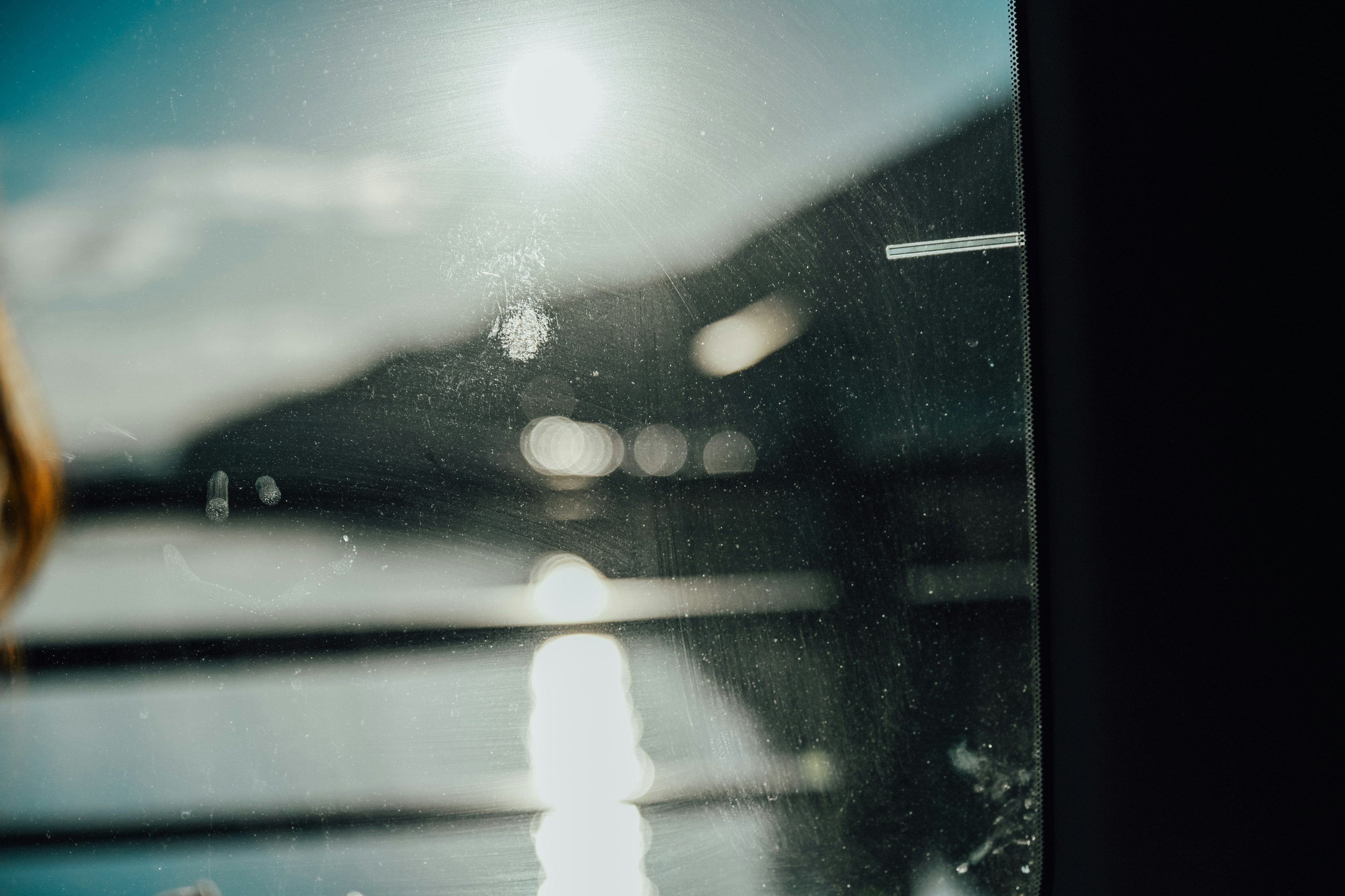 Vista de la superficie del agua y montañas a través de una ventana con fondo borroso y reflejos de luz