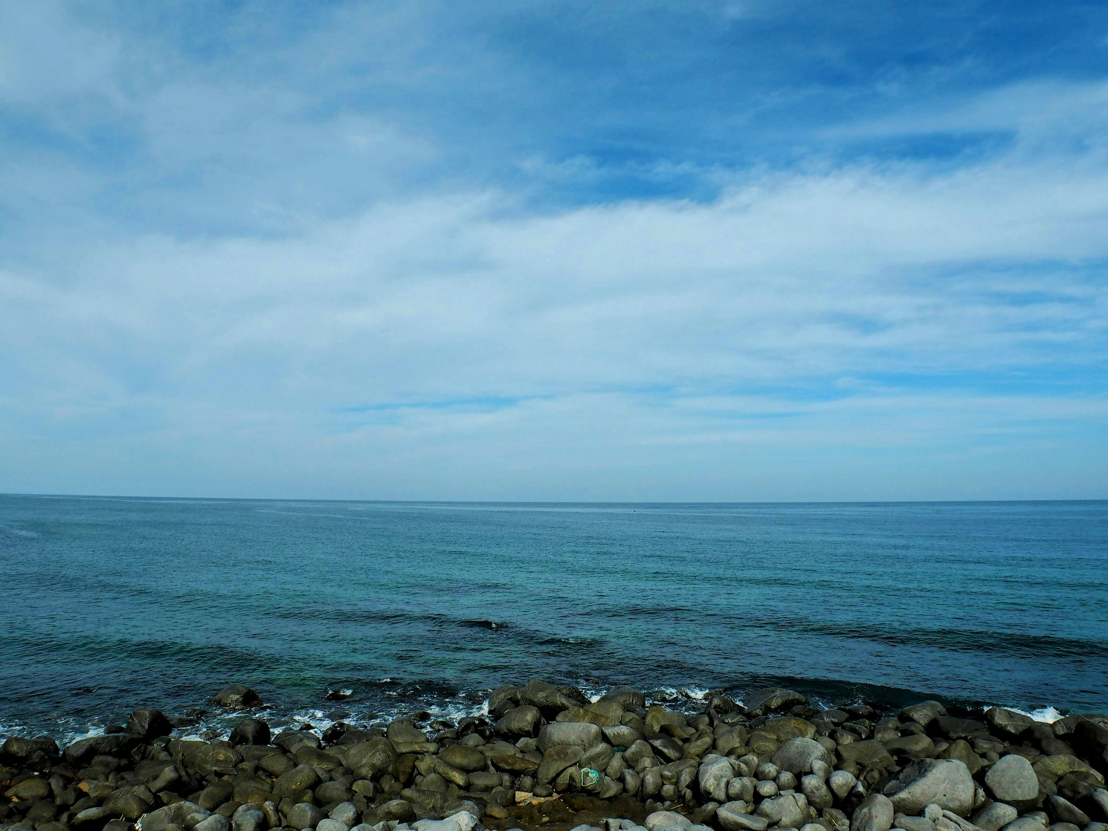 Pemandangan laut biru dan langit berawan dengan garis pantai berbatu