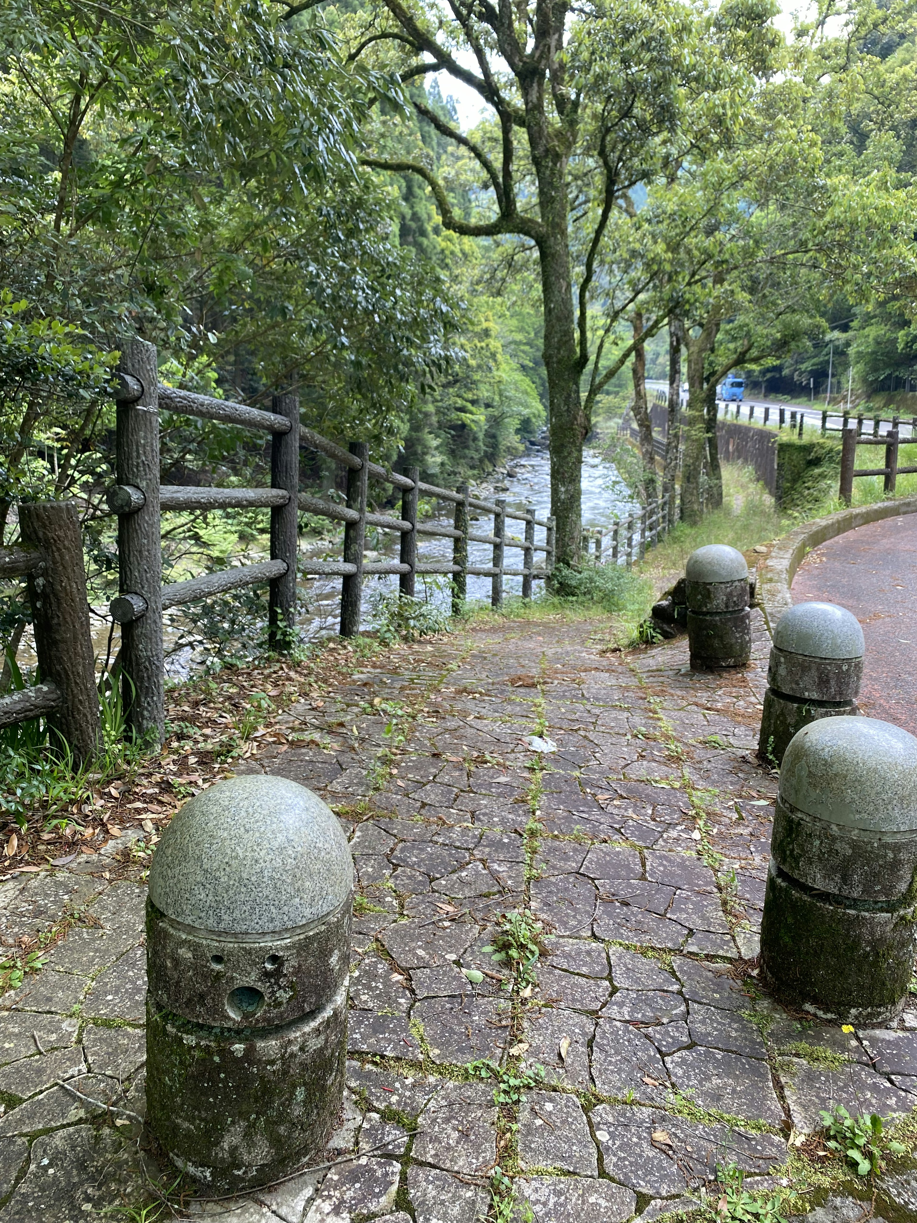 緑の木々に囲まれた小道にある丸い石のポール