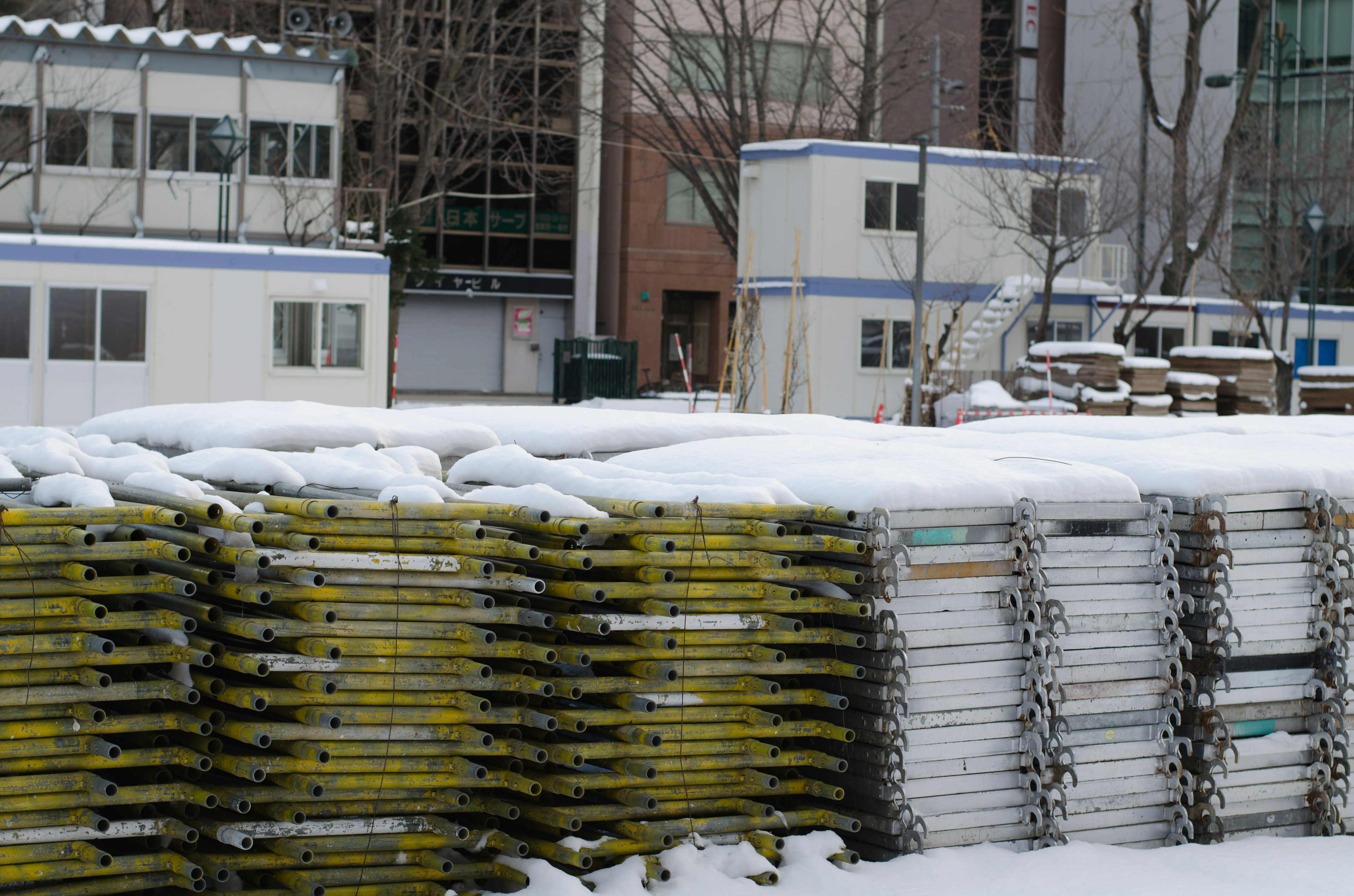 Andamios de construcción cubiertos de nieve apilados con edificios al fondo