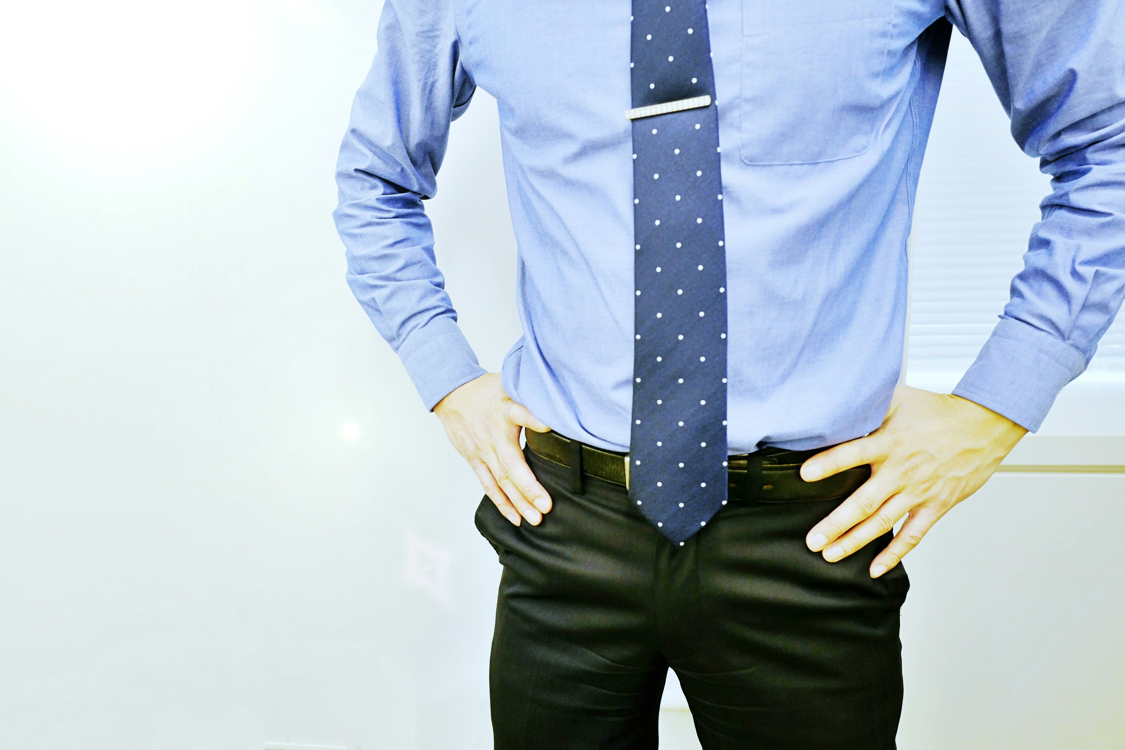 Hombre con camisa azul y corbata de lunares con las manos en las caderas