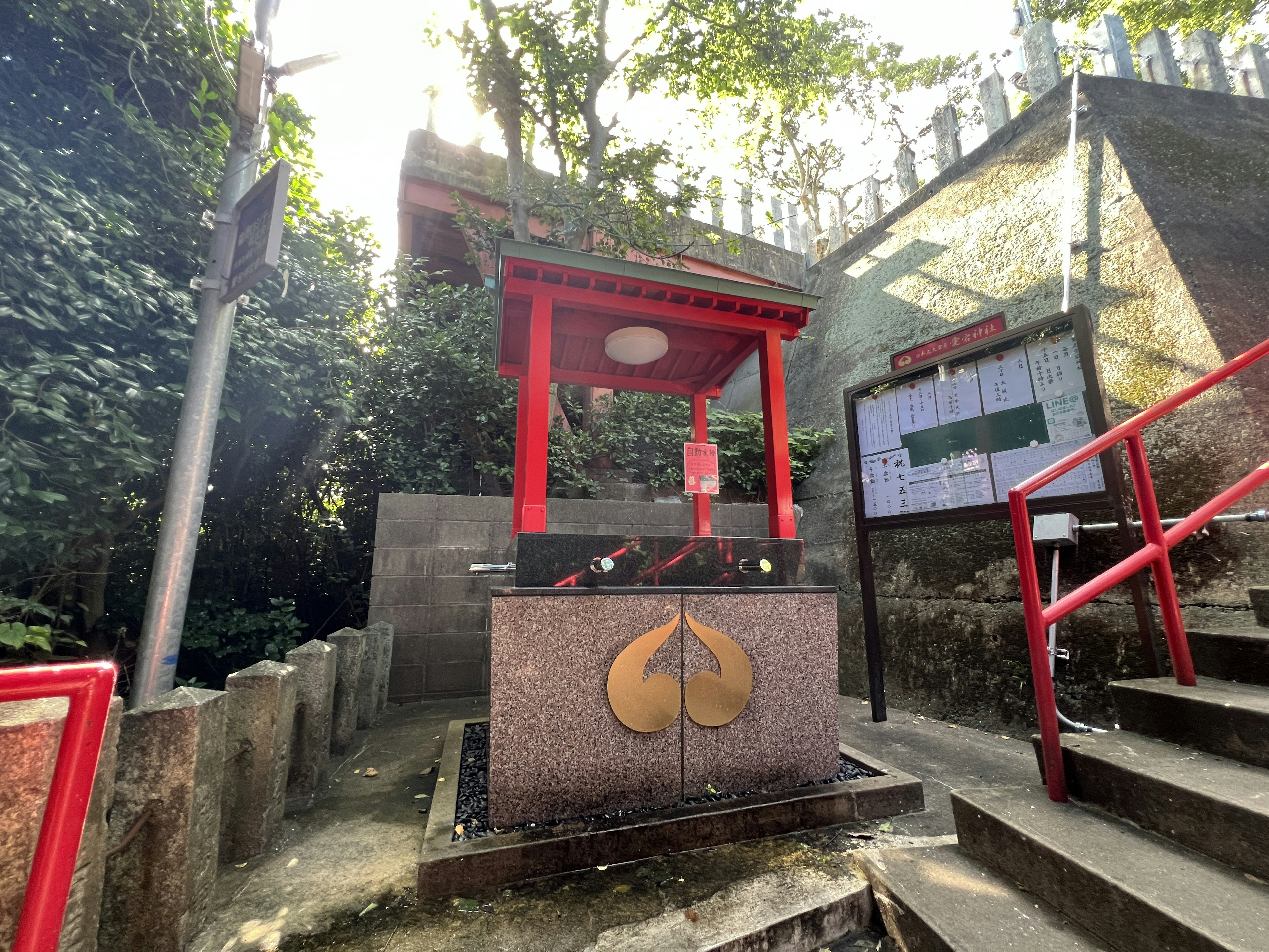 Water shrine with a red torii gate stone base featuring a leaf design surrounded by greenery