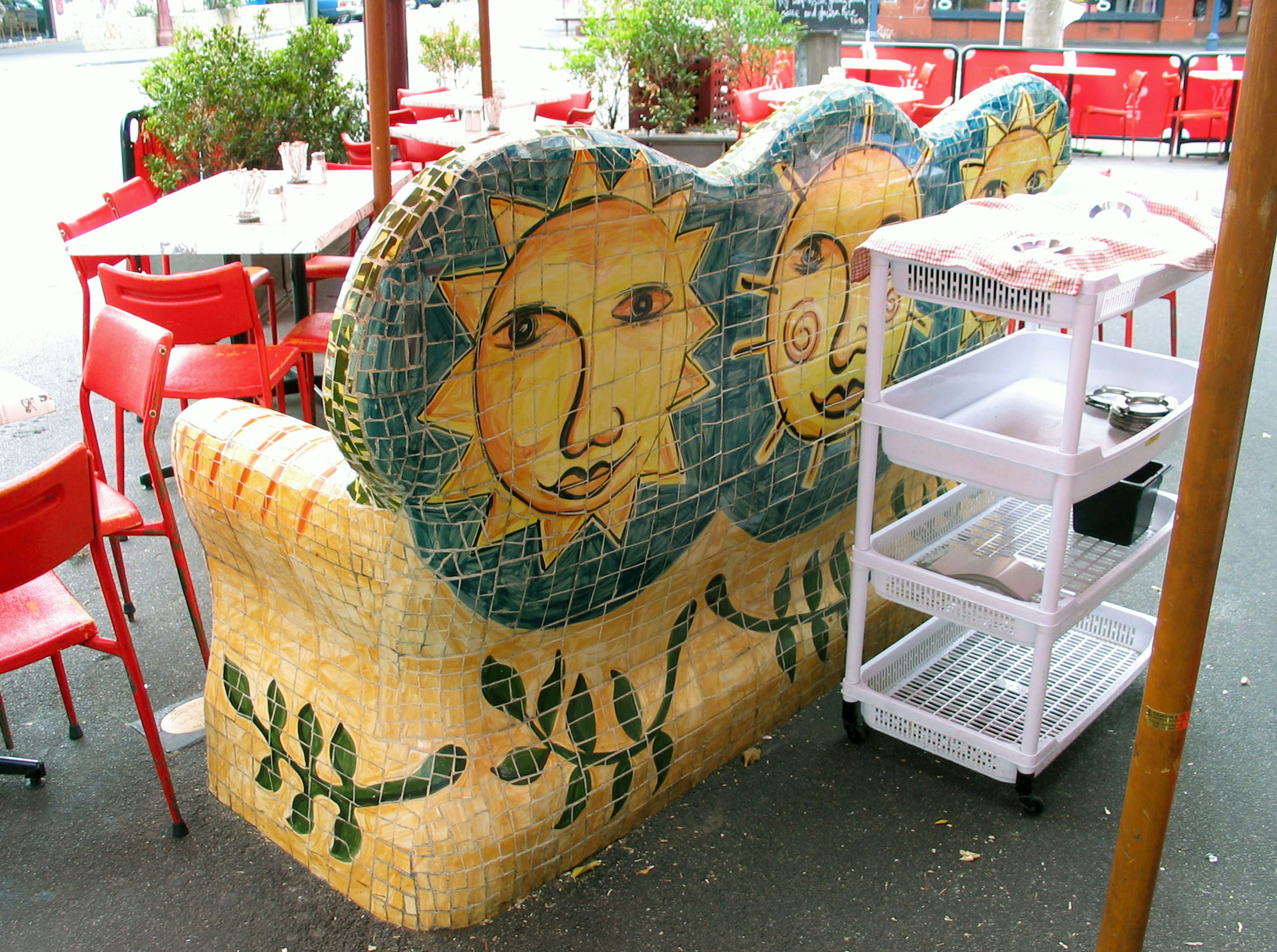 Banc en mosaïque coloré avec des visages de soleil et des chaises rouges dans un café en plein air