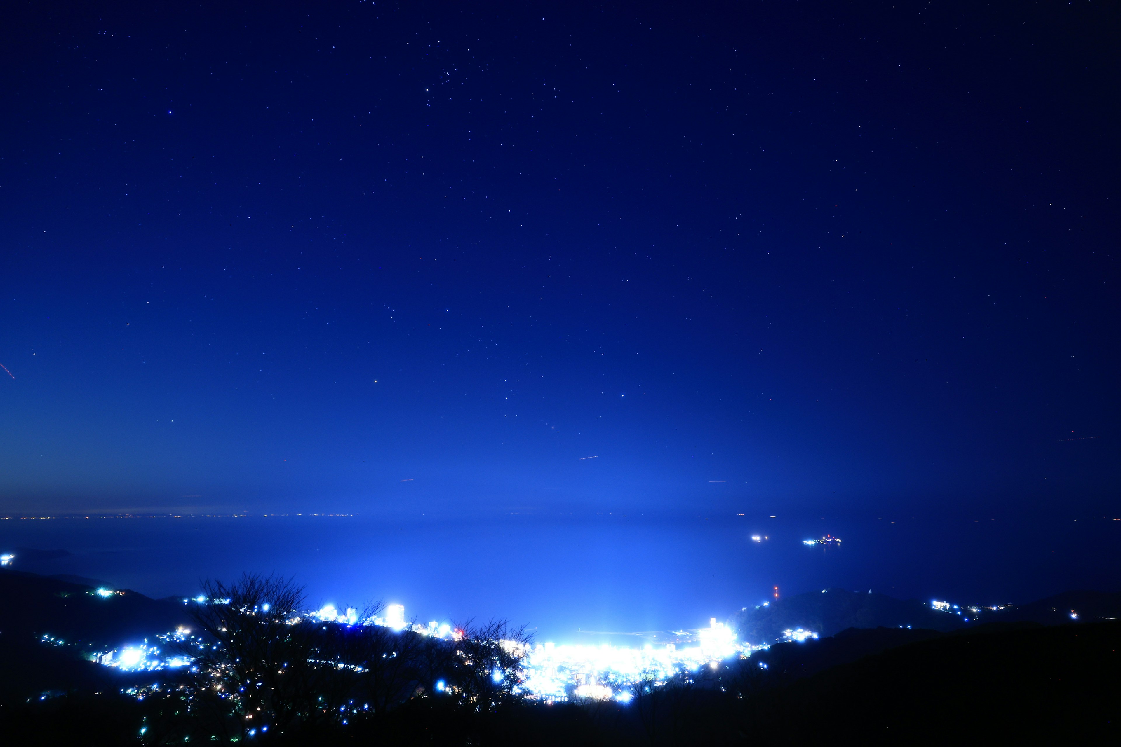 Nachthimmel voller Sterne und eine Stadt, die von blauen Lichtern beleuchtet wird