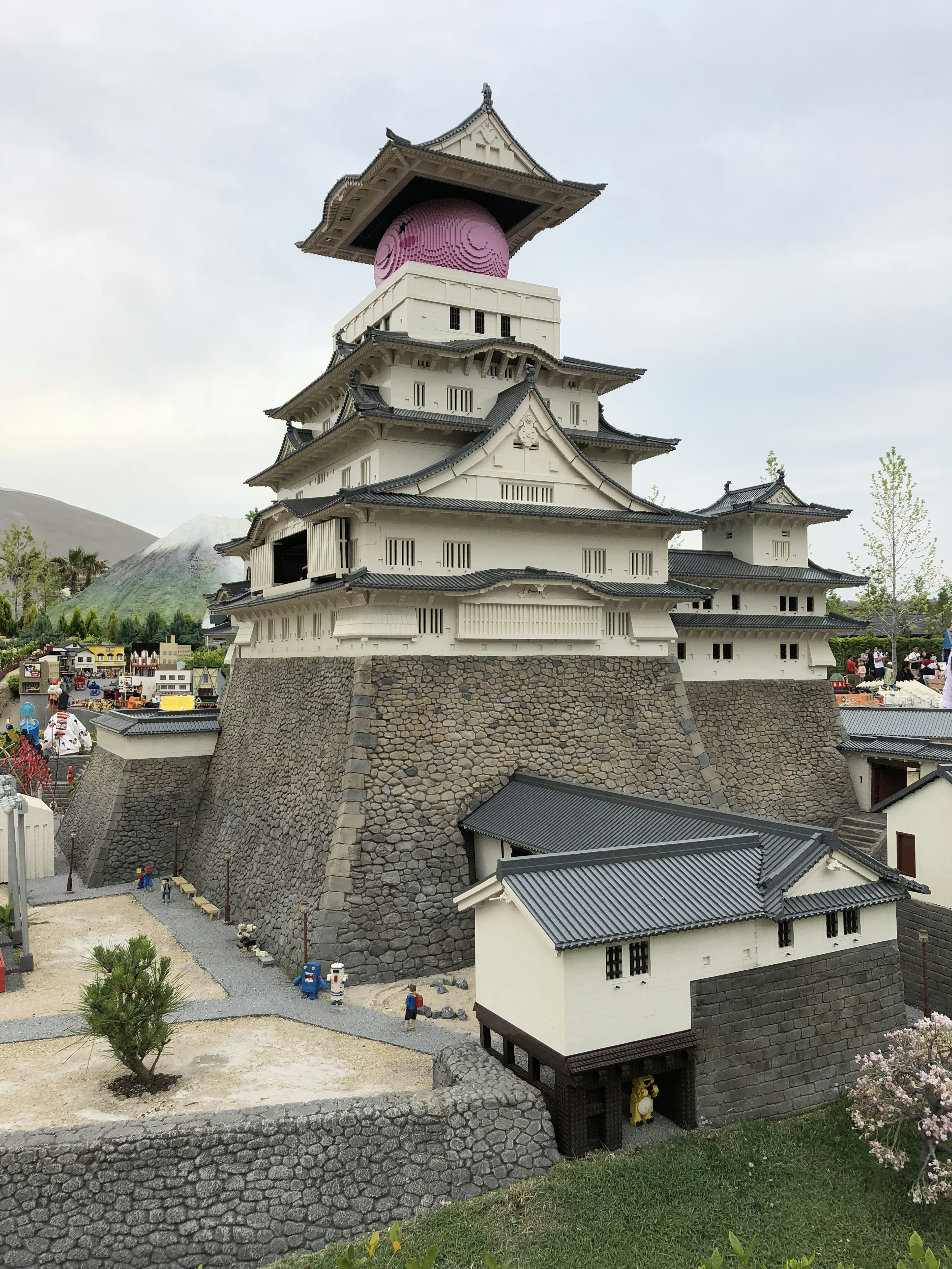 ピンクの屋根を持つ城の模型 周囲に小さな建物と緑の植物