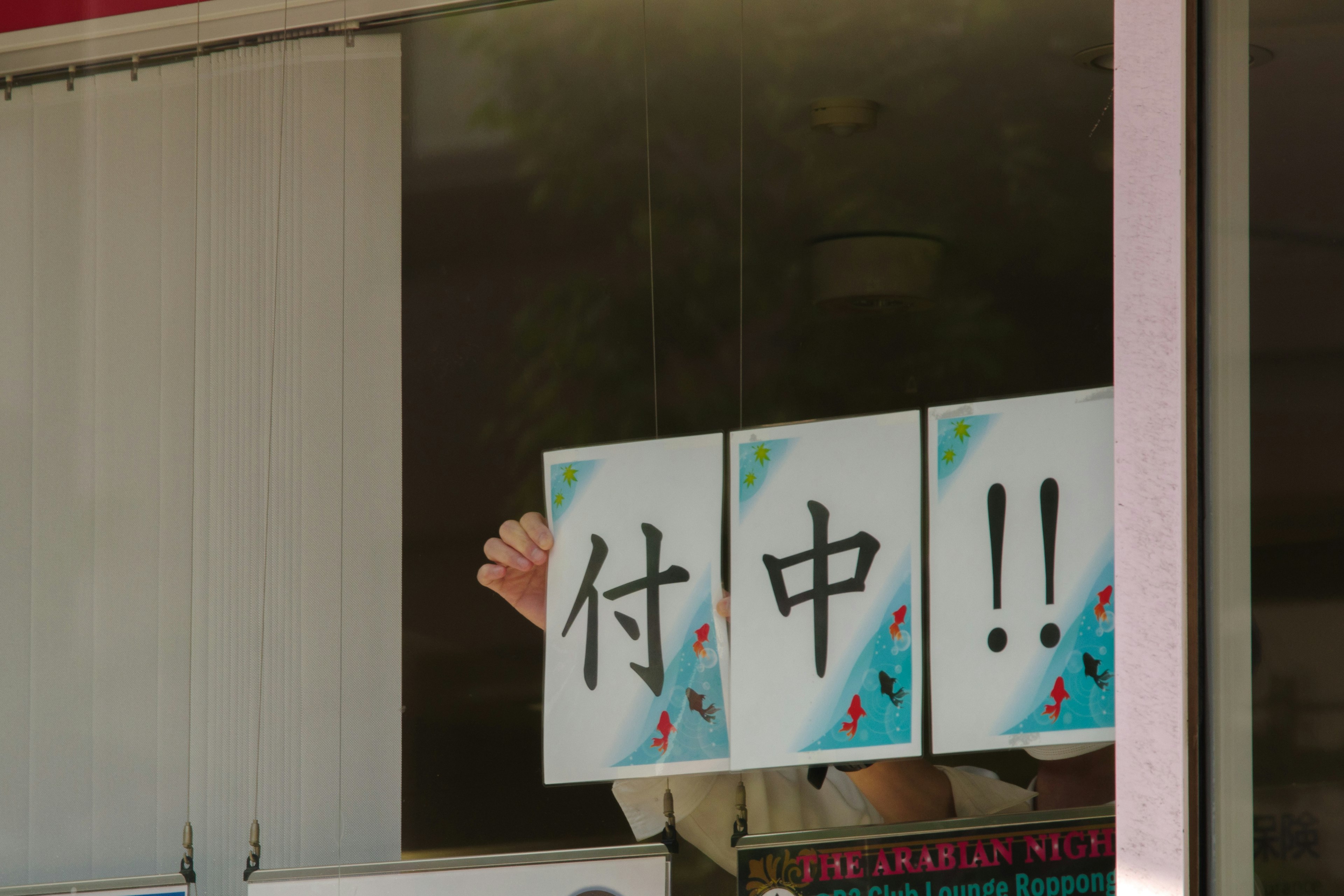 Hand visible from the window holding a sign saying '付中!!'