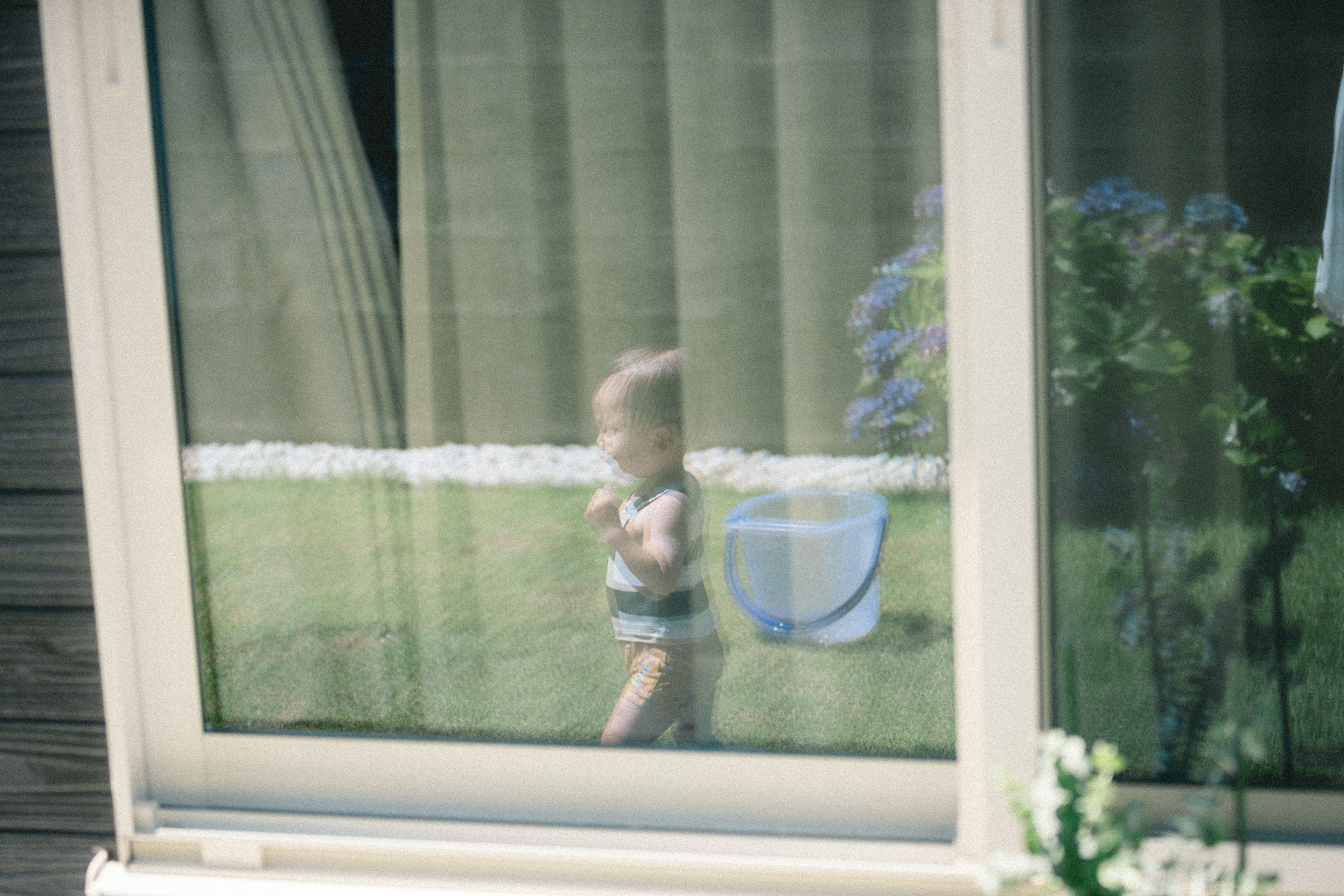 Kleinkind, das draußen spielt, durch ein Fenster gesehen